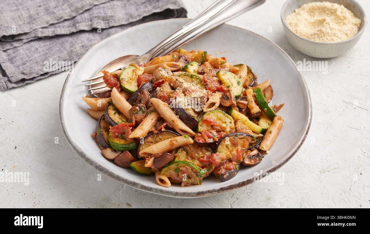 Penne con melanzane e zucchine. Un piatto di penne in stile mediterraneo con melanzane arrostite e zucchine, un gustoso pasto vegetariano. Foto Stock