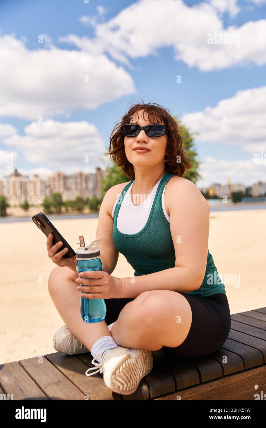 Una donna sorridente si diverte al sole, seduto su una panchina con un drink in mano. Foto Stock