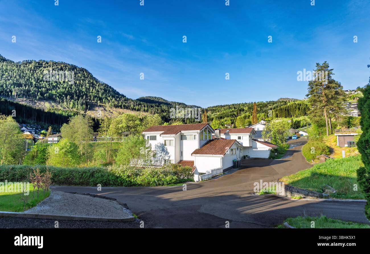 Area residenziale con case bianche circondate da vegetazione lussureggiante e un'atmosfera tranquilla, annidata vicino alle verdi montagne sotto un cielo blu limpido, evocativo Foto Stock