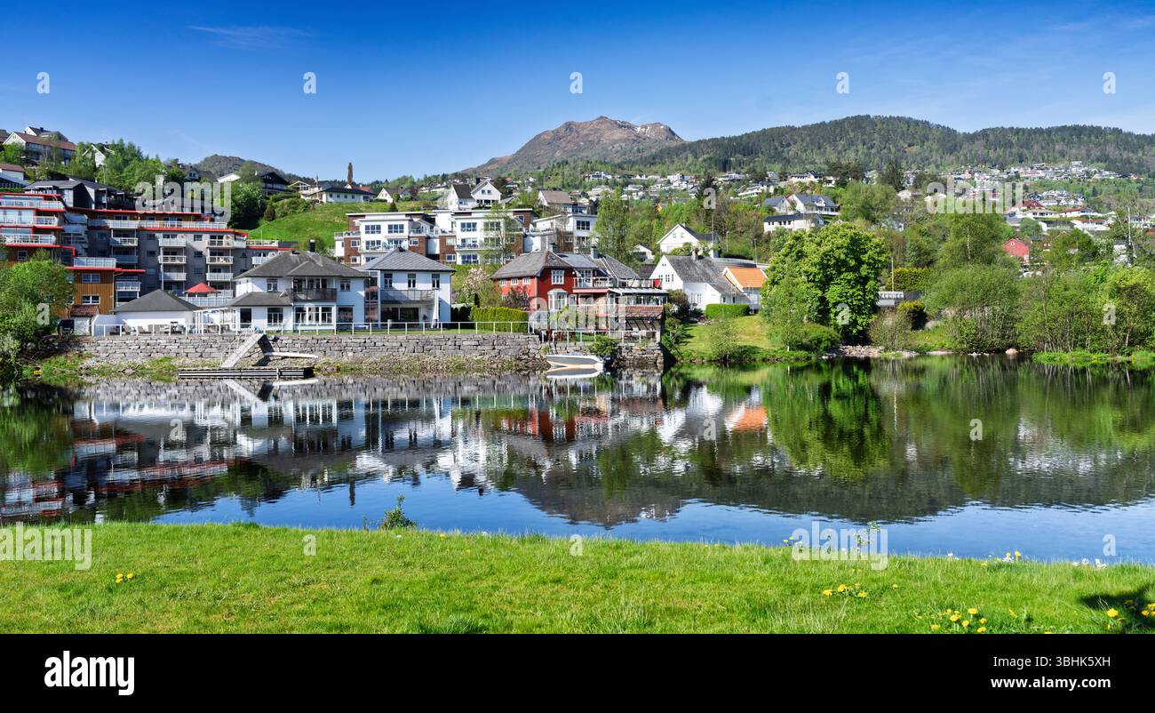 Città idilliaca annidata da un tranquillo lago di montagna, che mostra splendidi riflessi con vegetazione lussureggiante, acque calme e un'atmosfera pittoresca su un vib Foto Stock