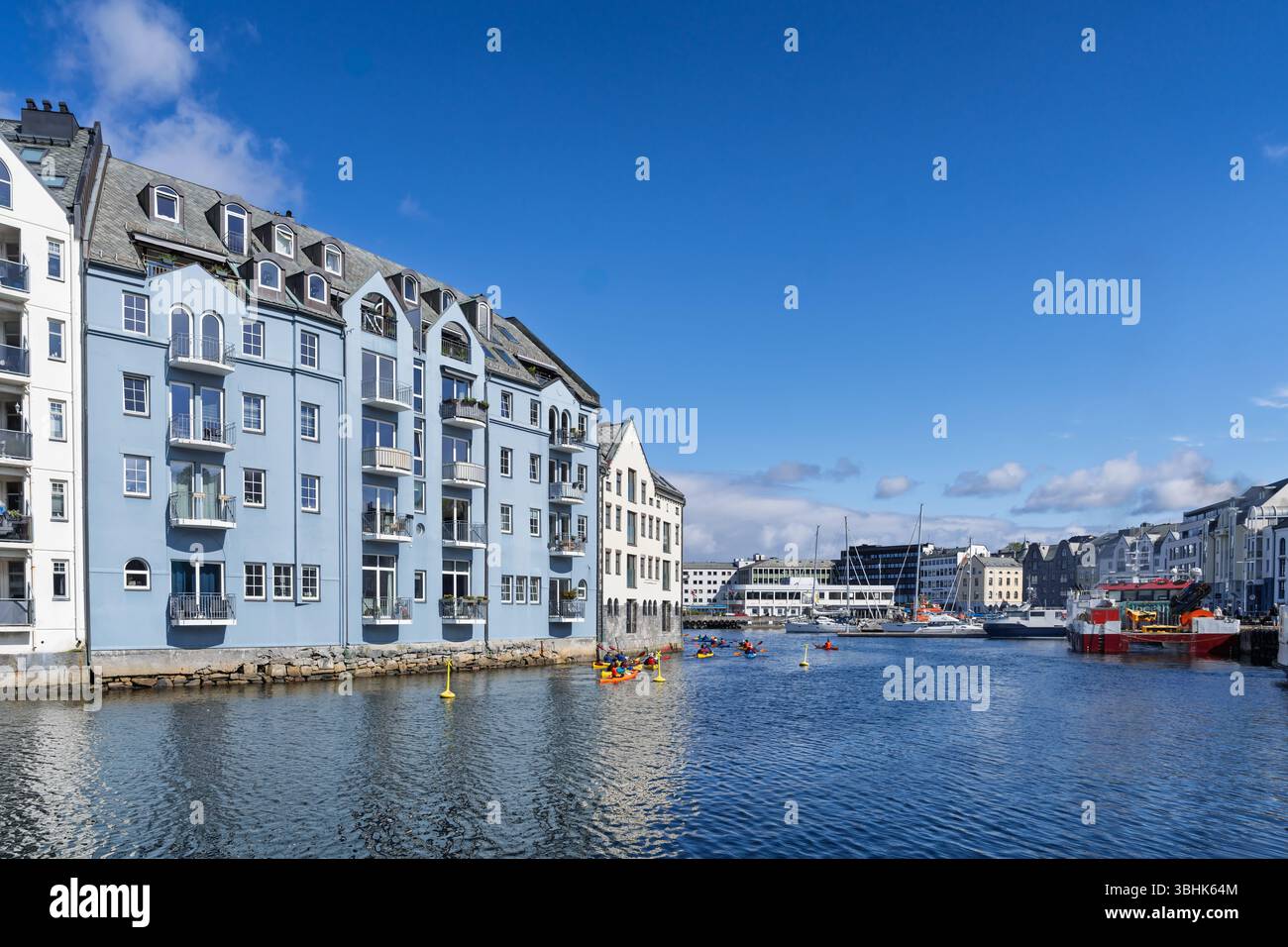 Incantevole vista di edifici colorati lungo un lungomare, sotto cieli azzurri. Le persone amano remare e kayak, creando un atmo vivace e vivace Foto Stock