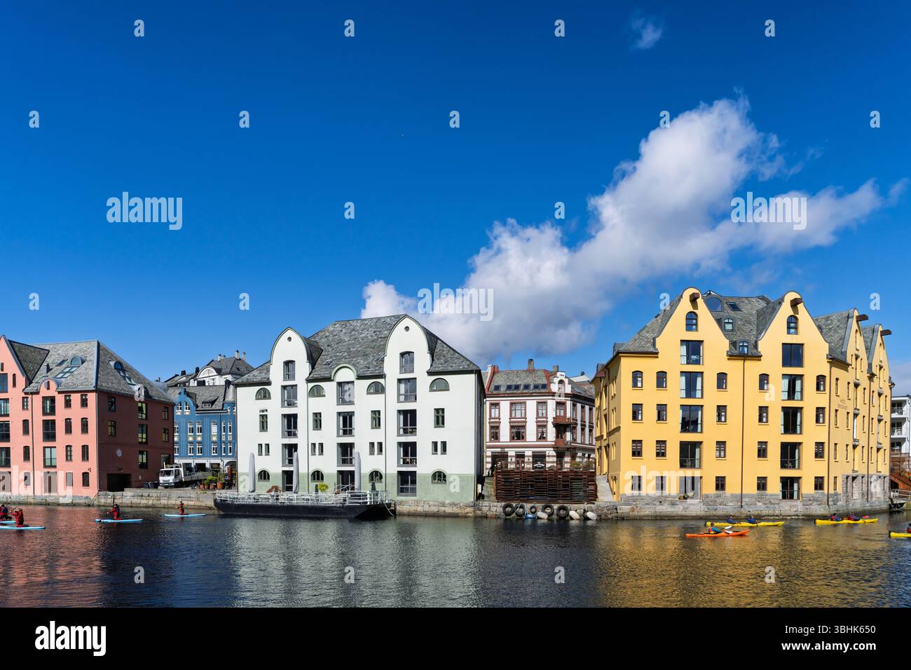 Incantevole vista di edifici colorati lungo un lungomare, sotto cieli azzurri. Le persone amano remare e kayak, creando un atmo vivace e vivace Foto Stock