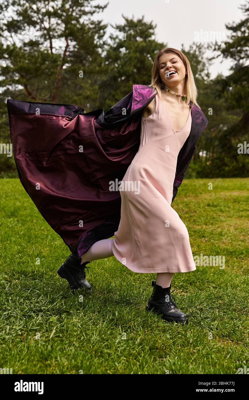 Una bella giovane donna con un vestito rosa chiaro e un mantello corre allegramente su un prato erboso. Foto Stock