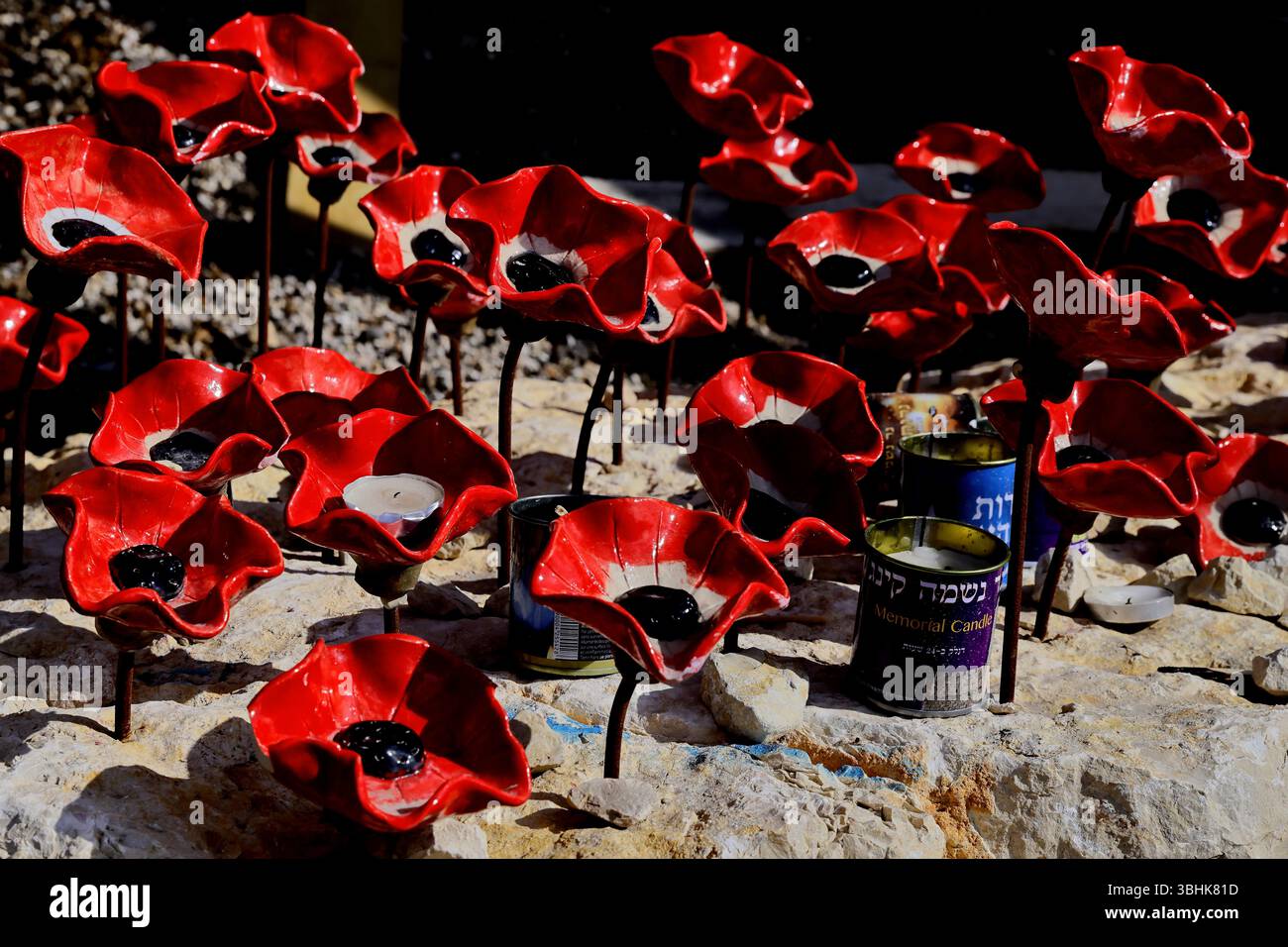 I papaveri in ceramica circondano le candele commemorative su pietra pallida presso il sito Car Wall, i loro petali rossi e i centri neri evocano solenni tributo e vivida memoria Foto Stock
