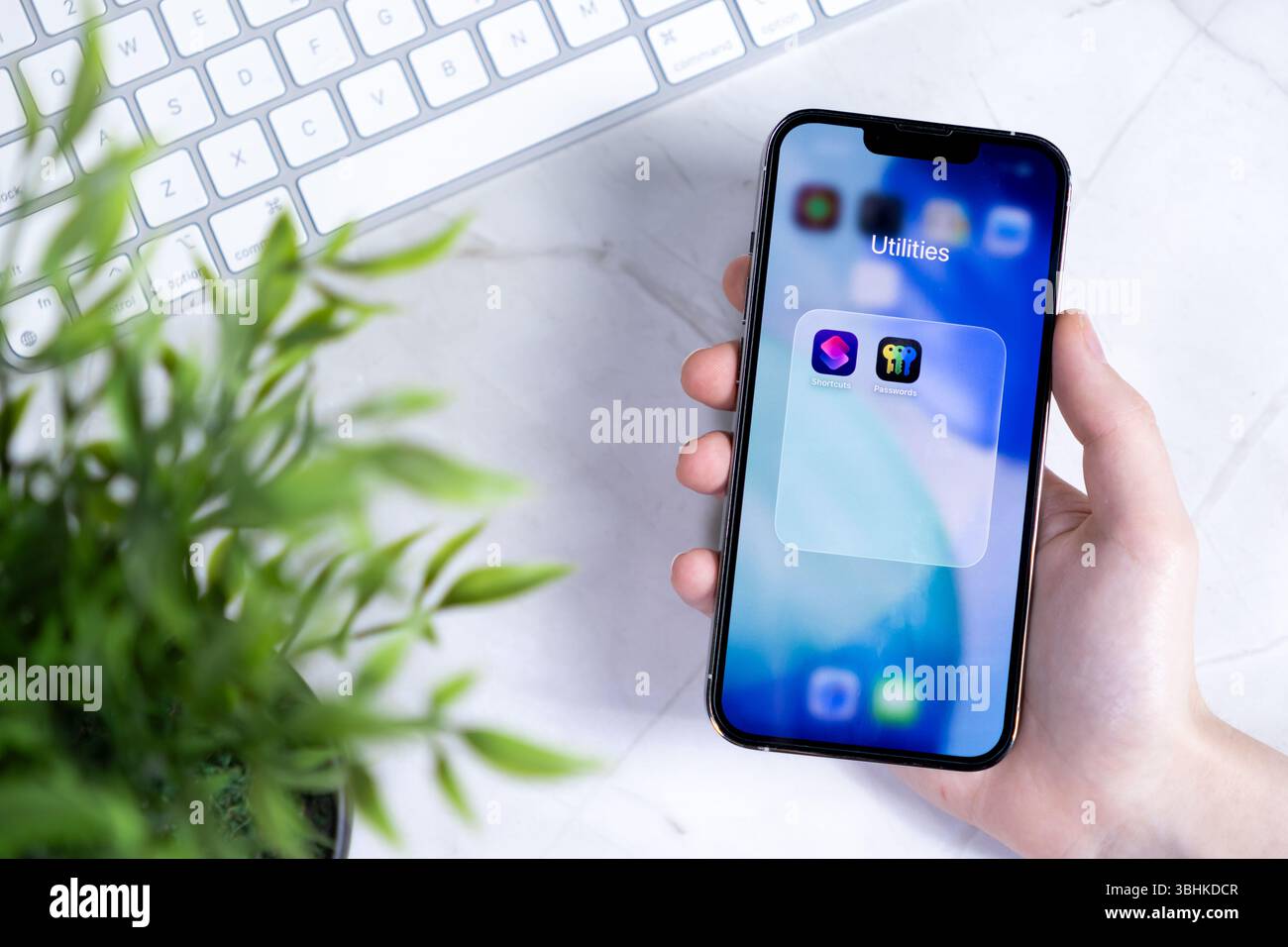 Poznan, Polonia - 10 giugno 2025: Primo piano di mano che regge uno smartphone contemporaneo, con la cartella Utilità con le app del nuovo iOS 26 Liquid Foto Stock