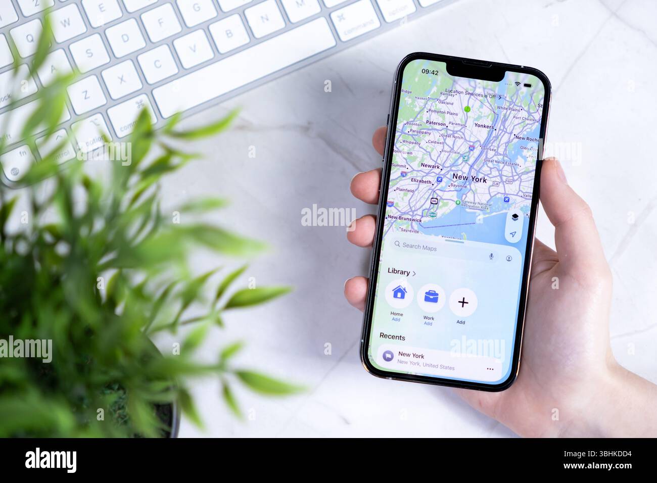 Poznan, Polonia - 10 giugno 2025: Una mano regge uno smartphone moderno con il nuovo design iOS 26 e Liquid Glass, che mostra la mappa dettagliata di New York per Advan Foto Stock