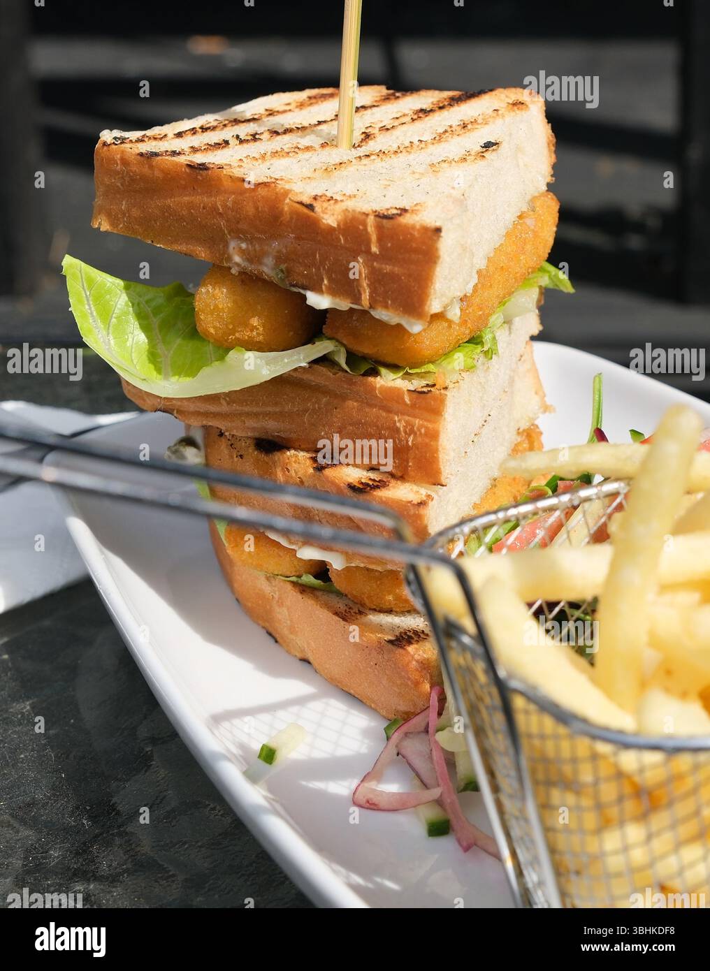 Gustoso sandwich di pesce con patatine fritte e insalata su un piatto bianco. Foto Stock