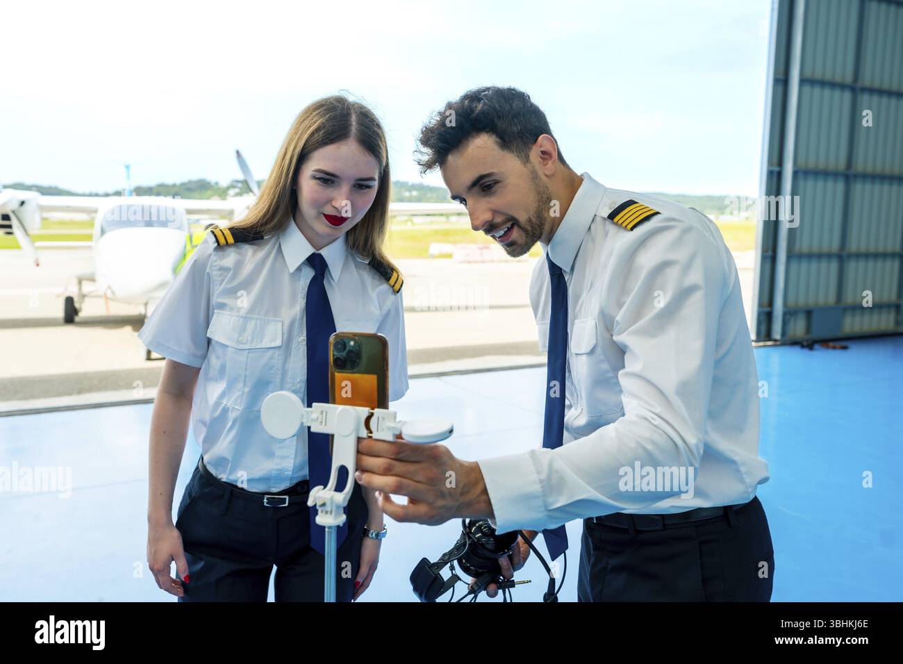 Due piloti stanno utilizzando uno smartphone e un anemometro per controllare le condizioni meteorologiche all'interno di un hangar dell'aeromobile Foto Stock