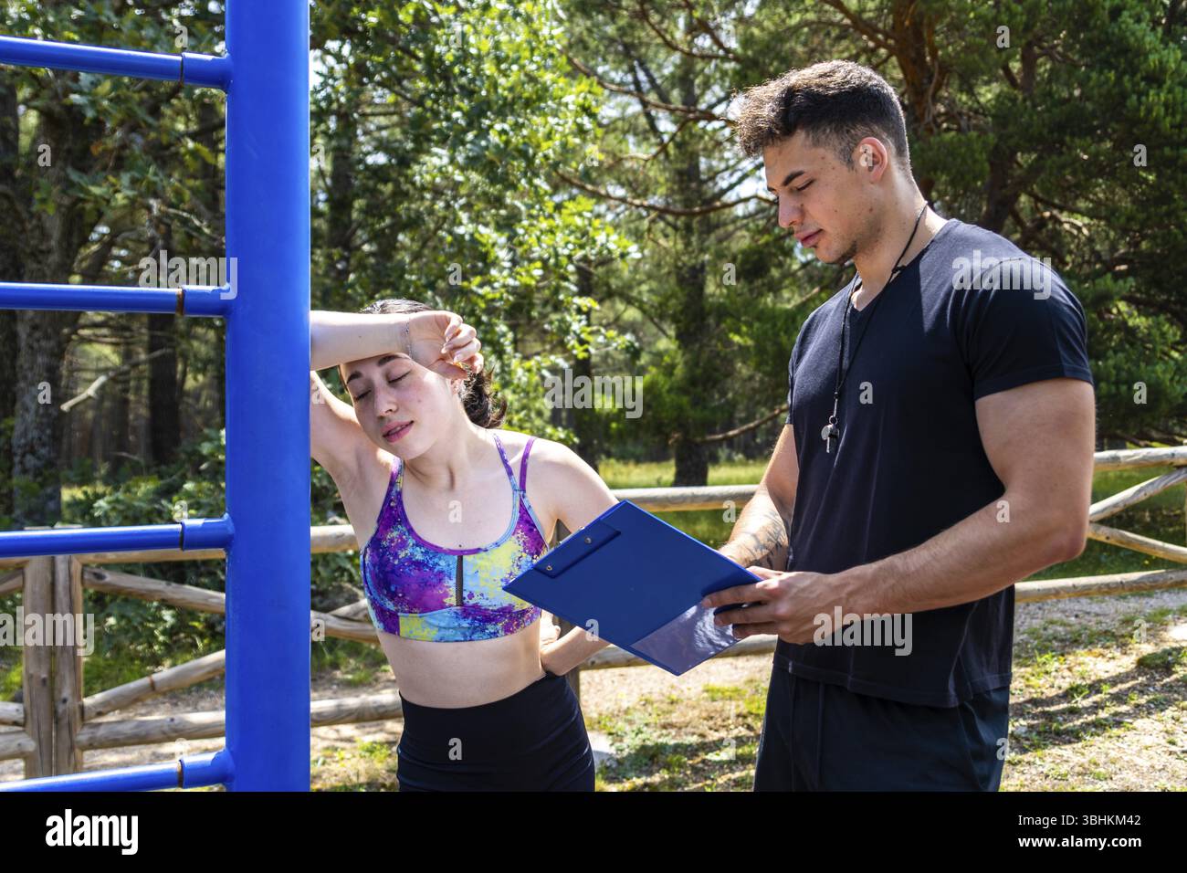 Ritratto di una donna sportiva che si riposa mentre riceve istruzioni per l'esercizio dal suo personal trainer all'aperto Foto Stock
