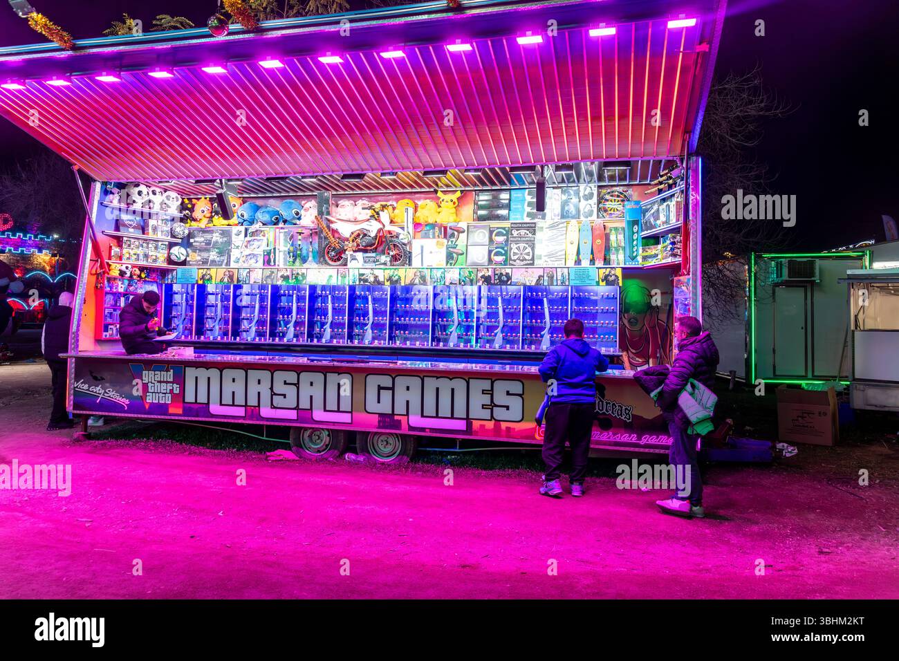 Barcellona, Catalogna - Spagna - 01-07-2025: Un luminoso stand fieristico con una serie di premi, giochi arcade e illuminazione al neon in un carnevale notturno. Foto Stock