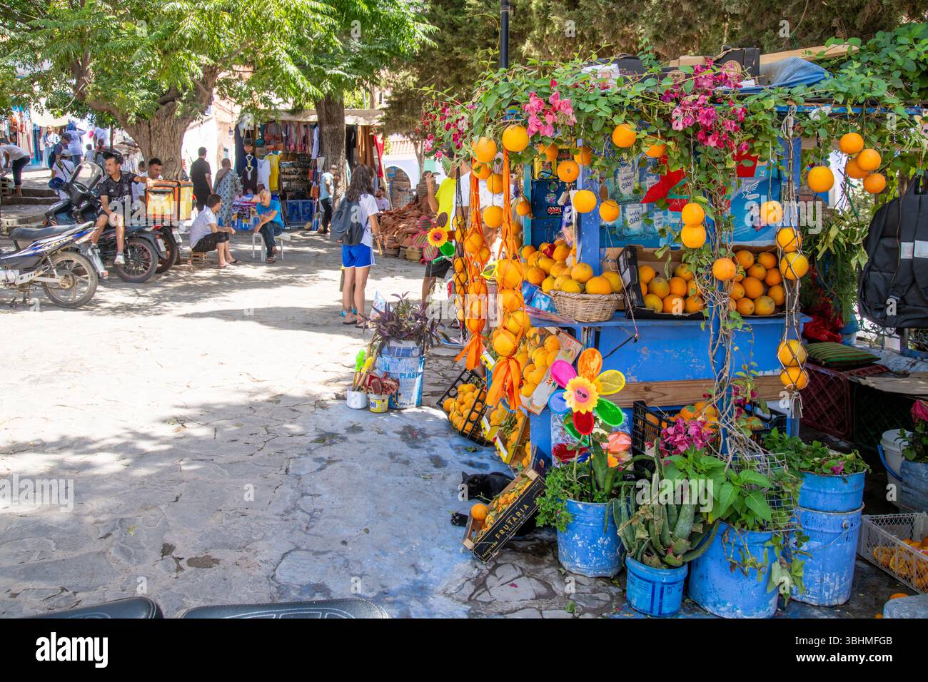 Chefchaouen, Chefchaouen - Marocco - 08-20-2024; scena di strada a Chefchaouen con una bancarella di mercato che offre frutta e fiori d'arancia, circondata da blu Foto Stock