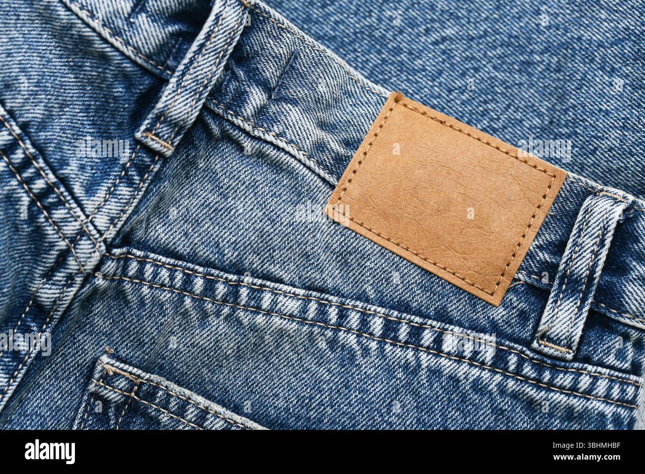 Jeans blu denim con toppa marrone in pelle. Dettagli tasca posteriore. Elegante texture di abbigliamento alla moda. Concetto di stile urbano informale. Primo piano di pantaloni in tessuto. Foto Stock