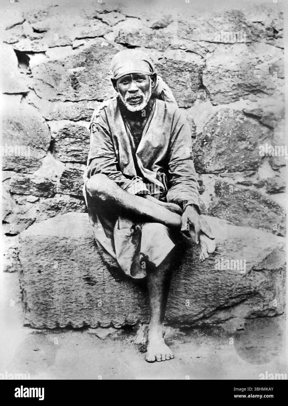 Fotografia in bianco e nero dell'insegnante spirituale indiano e di san Sai Baba di Shirdi seduta su una pietra intorno al 1915, Shirdi Sai Baba Foto Stock