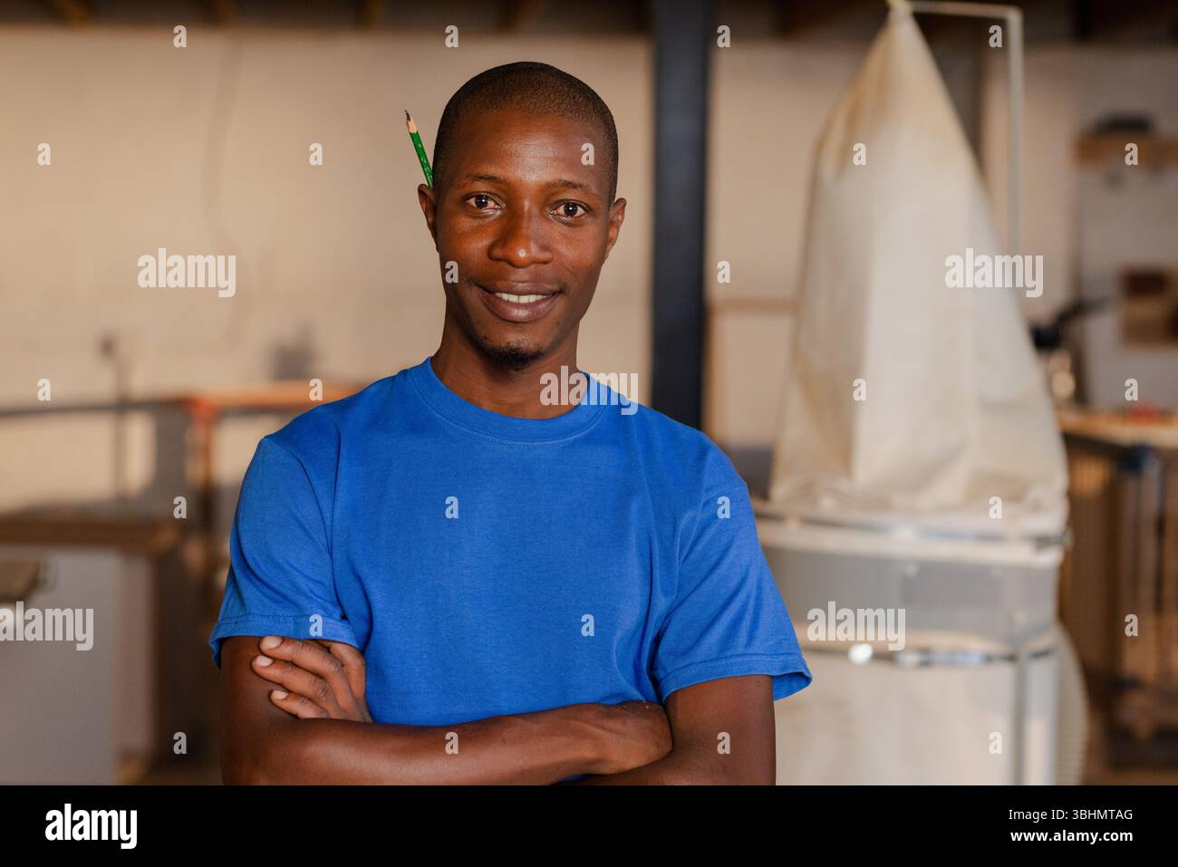 Uomo afroamericano medio adulto in piedi in un negozio di legno tenendo una matita dietro l'orecchio vicino al collettore di polvere Foto Stock
