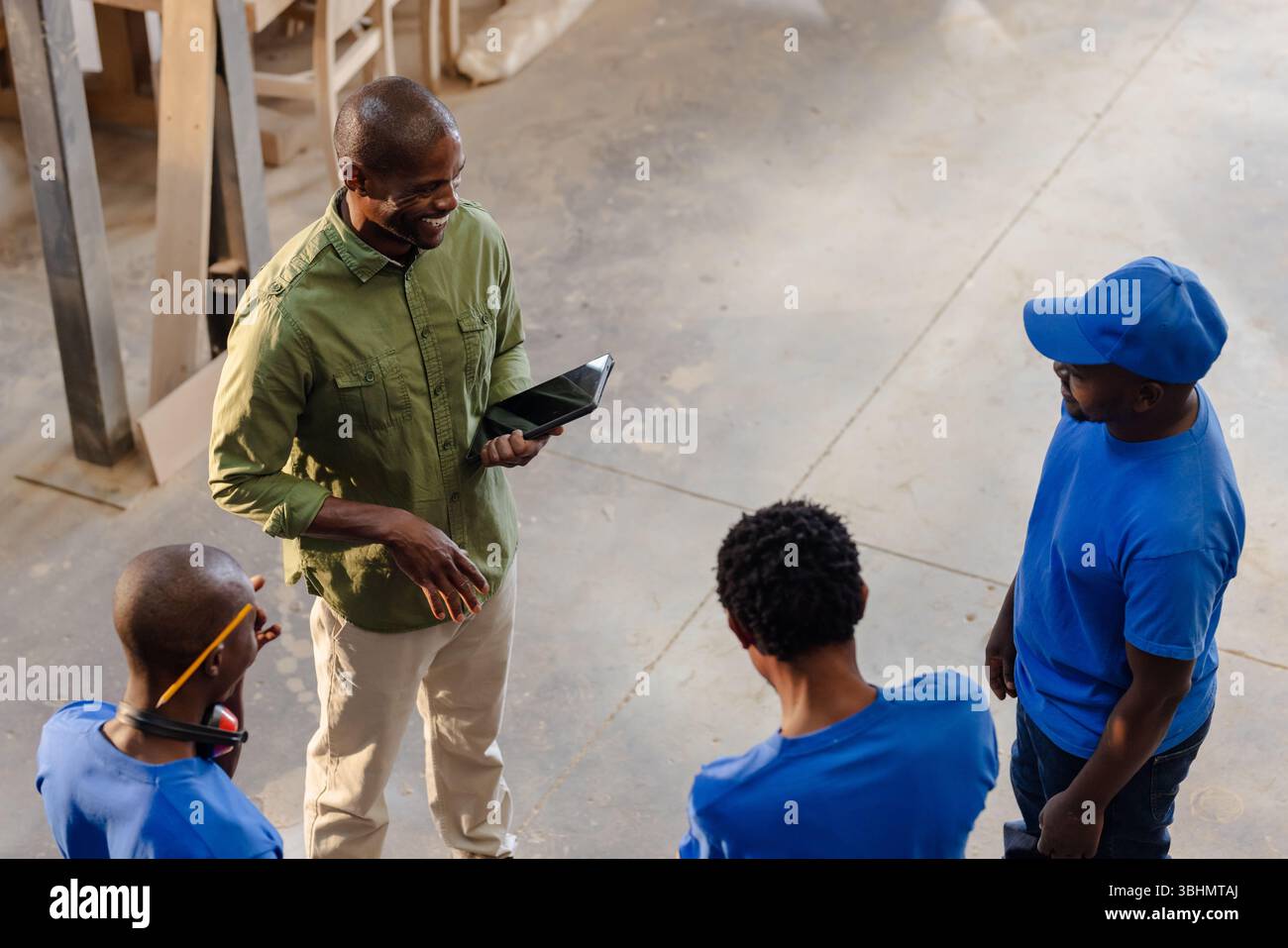Uomini afroamericani che discutono piani di lavoro in officina con tavoletta, tavole di legno Foto Stock