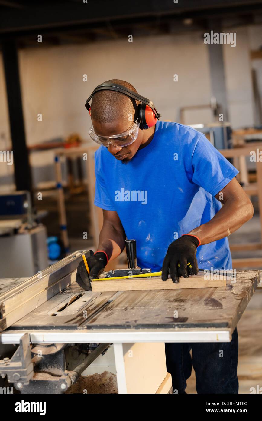Tavola di legno appoggiata sulla sega da tavolo sottoposta a misurazioni precise in un'officina di falegnameria molto frequentata Foto Stock
