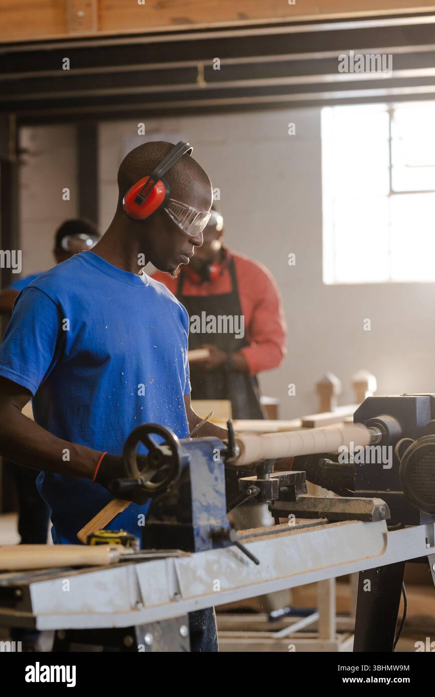 I colleghi afroamericani che lavorano il cilindro di sagomatura del tornio in officina con occhiali di sicurezza Foto Stock