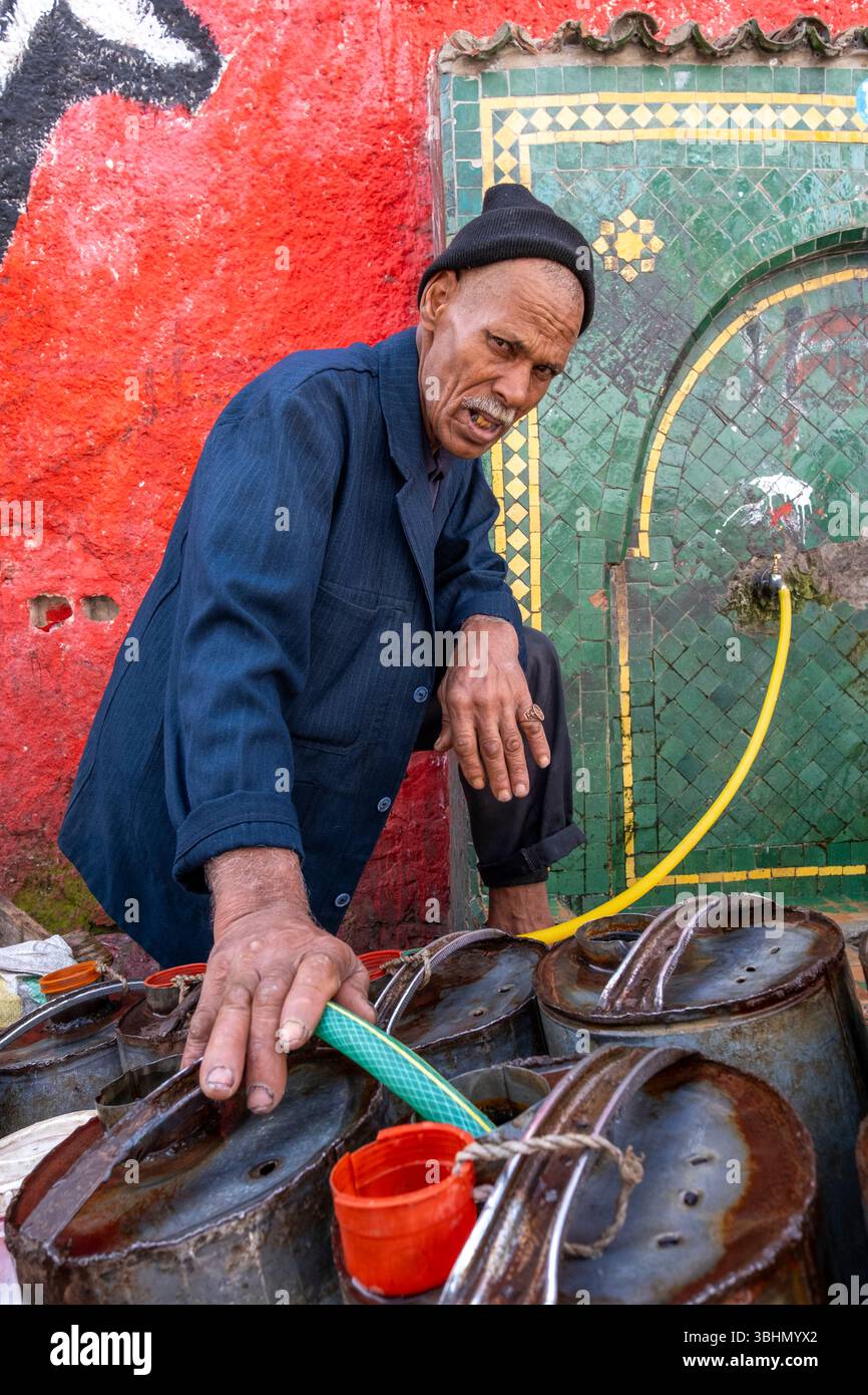 Un uomo immette acqua nei contenitori della Moschea Kasbah a Jemaael-Fnaa, bazar di Marrakech, Marocco. Foto Stock
