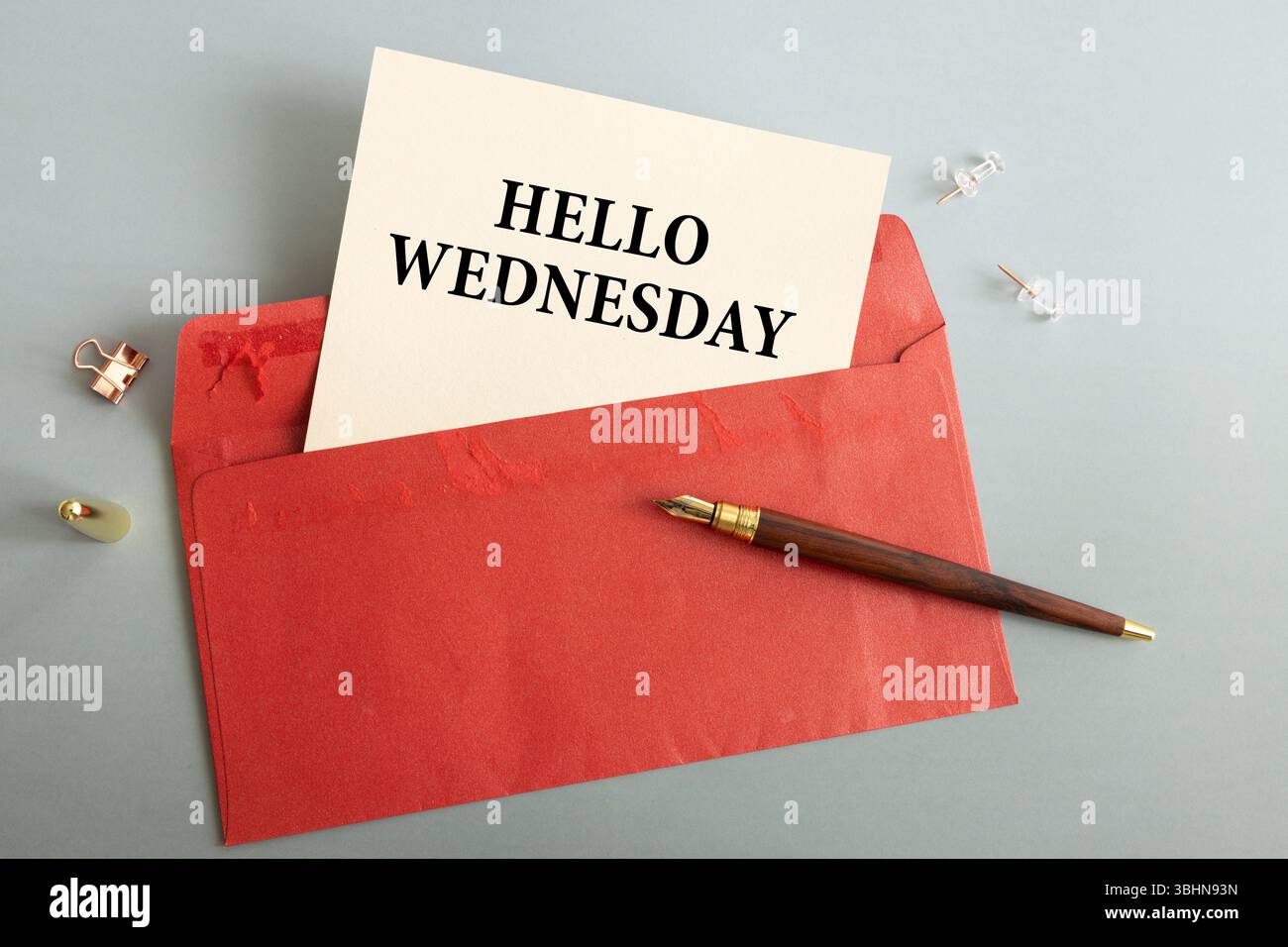 Su un tavolo di legno chiaro, c'è un ramo di eucalipto, una penna stilografica e un foglio di carta con il testo HELLO WEDNESDAY Foto Stock