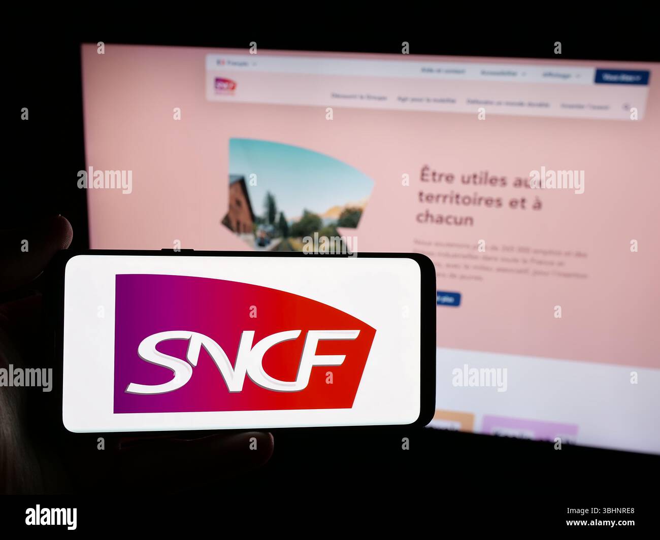 Stoccarda, Germania - 03-20-2025: Persona in possesso di smartphone con logo della società ferroviaria francese SNCF Group sullo schermo davanti al sito web. Foto Stock