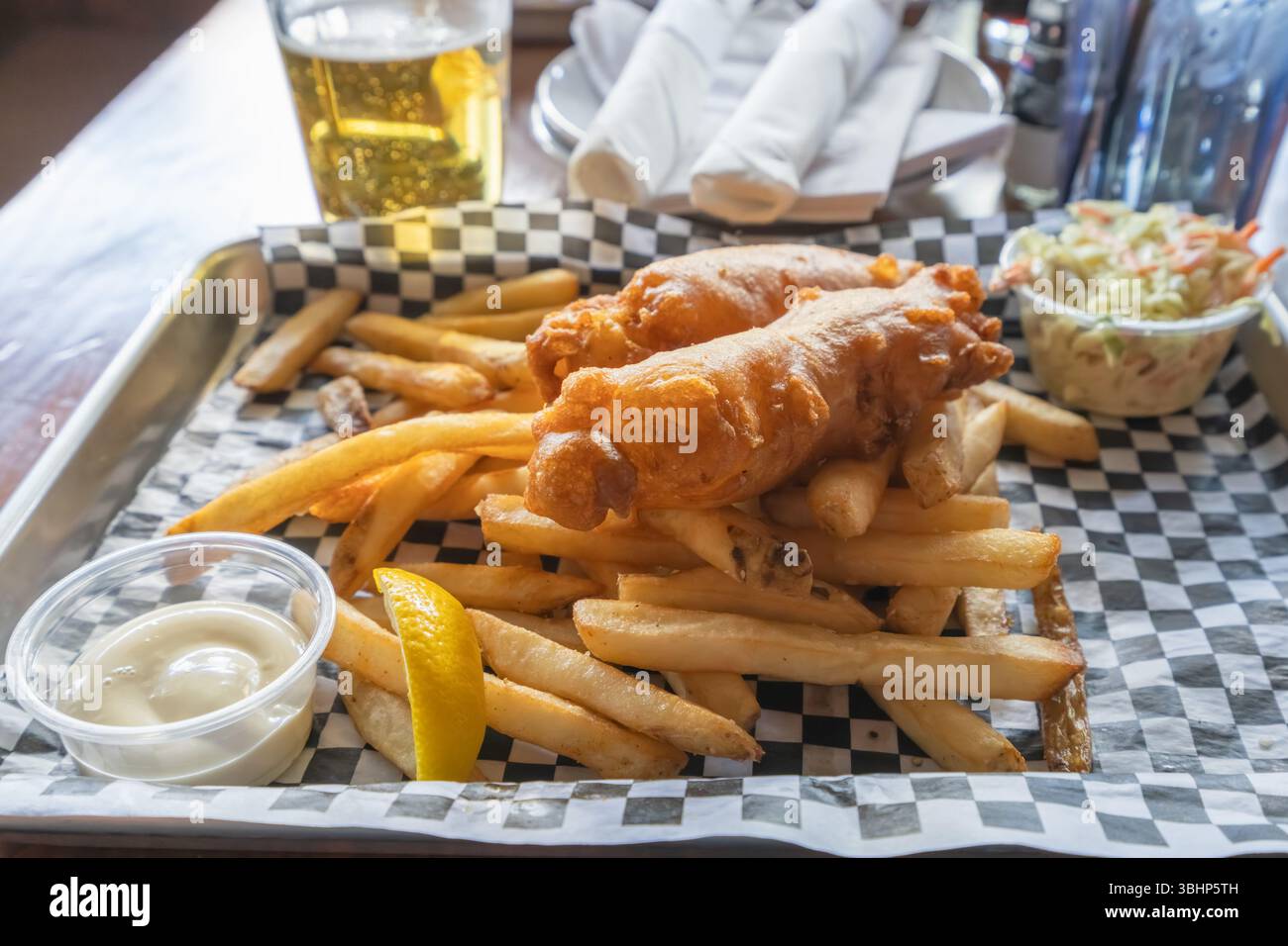 Fish and chips appena fritti con un lato di crema di insalata di cavolo e birra su un rustico tavolo di legno. Foto Stock
