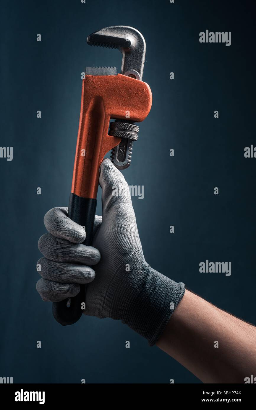 Gli idraulici indossano un guanto con una chiave stringitubo su sfondo blu Foto Stock