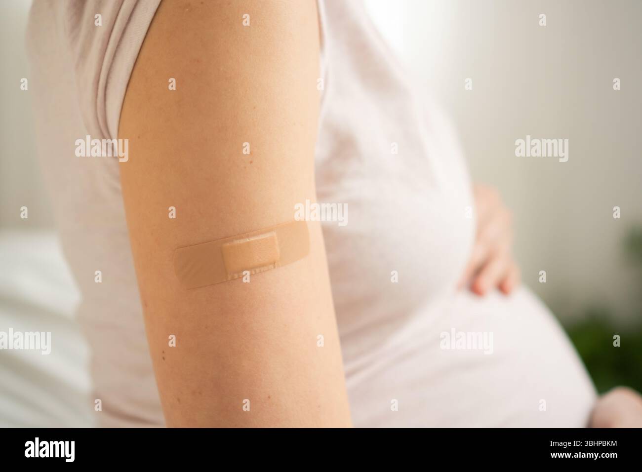 Vista dettagliata della bendatura di immunizzazione sull'avambraccio di una donna incinta. Assistenza sanitaria preventiva essenziale durante il periodo di gestazione. Foto Stock