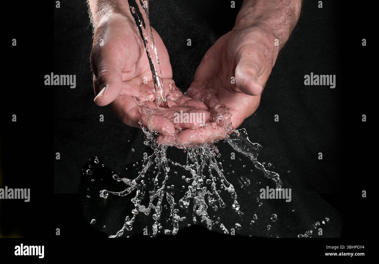 Mani che catturano l'acqua corrente che scorre con schizzi e scintillanti gocce su sfondo nero, concetto per le risorse ambientali, la salute e h Foto Stock