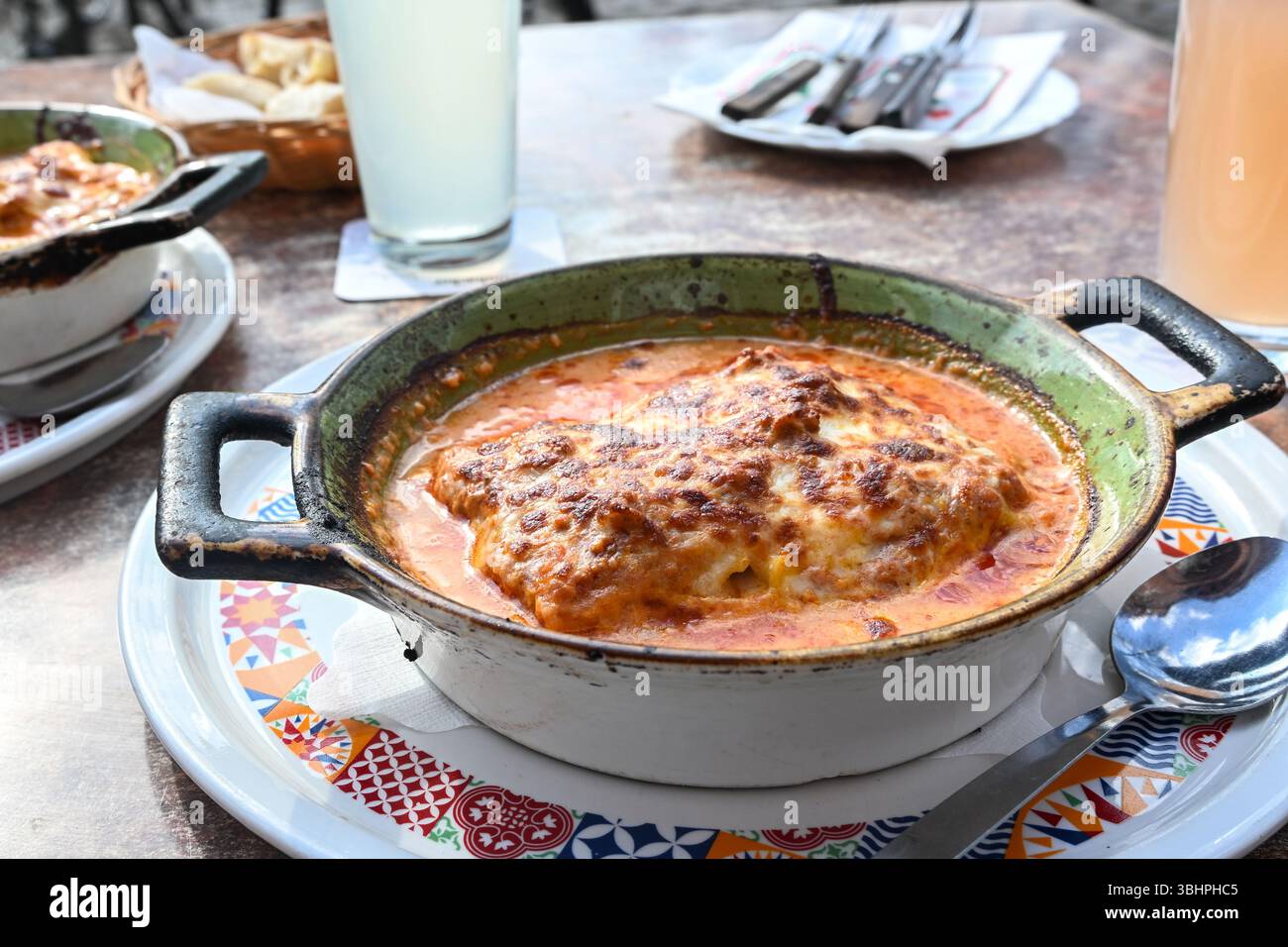 Lasagne, pasta italiana con carne macinata, salsa di pomodoro e mozzarella in una casseruola rustica in ceramica su un tavolo da pranzo in un ristorante, selezionato per Foto Stock