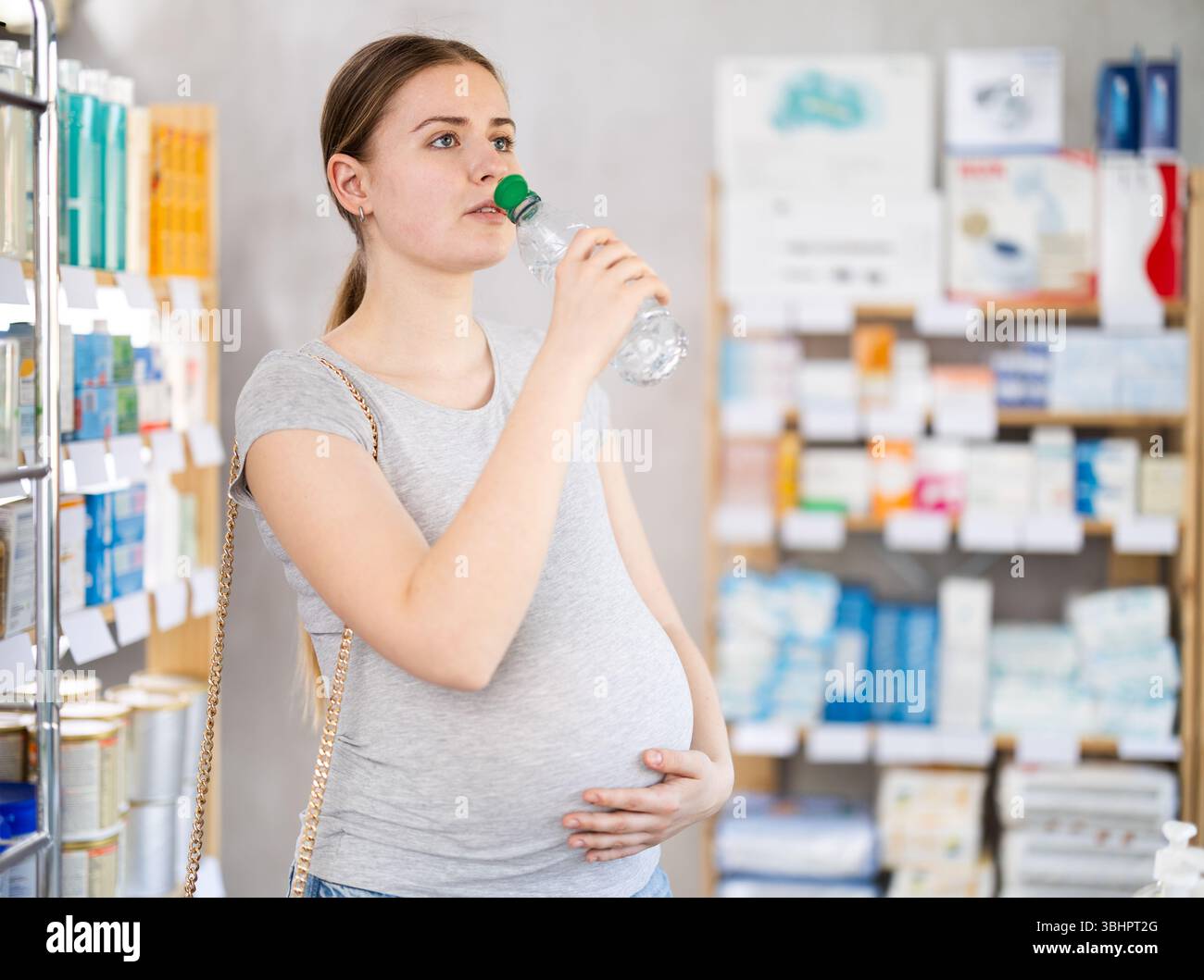 La ragazza incinta in farmacia beve l'acqua dalla bottiglia Foto Stock