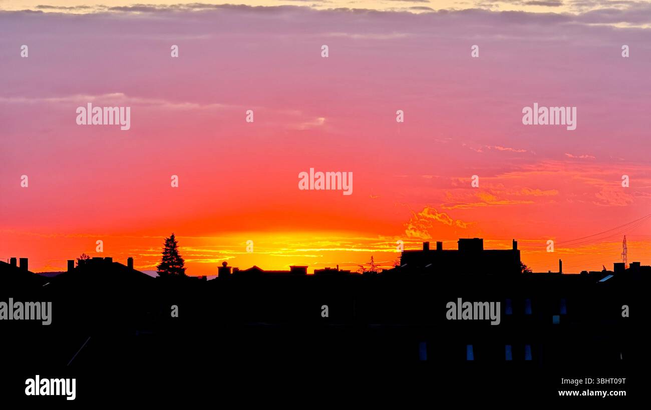 Tramonto colorato sullo skyline della città con vivaci sfumature di rosso, arancione e viola. Gli edifici sagomati contrastano con il suggestivo cielo serale. Foto Stock