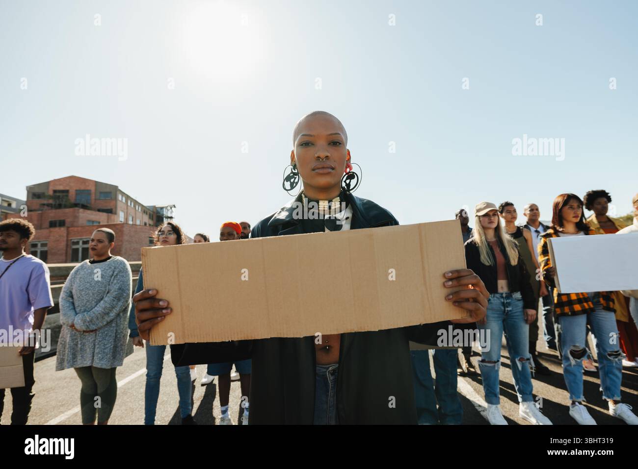 Un gruppo eterogeneo di persone che si riuniscono in una protesta di strada, guidata da una giovane donna fiduciosa con un cartello di cartone vuoto, che esprime solidarietà Foto Stock