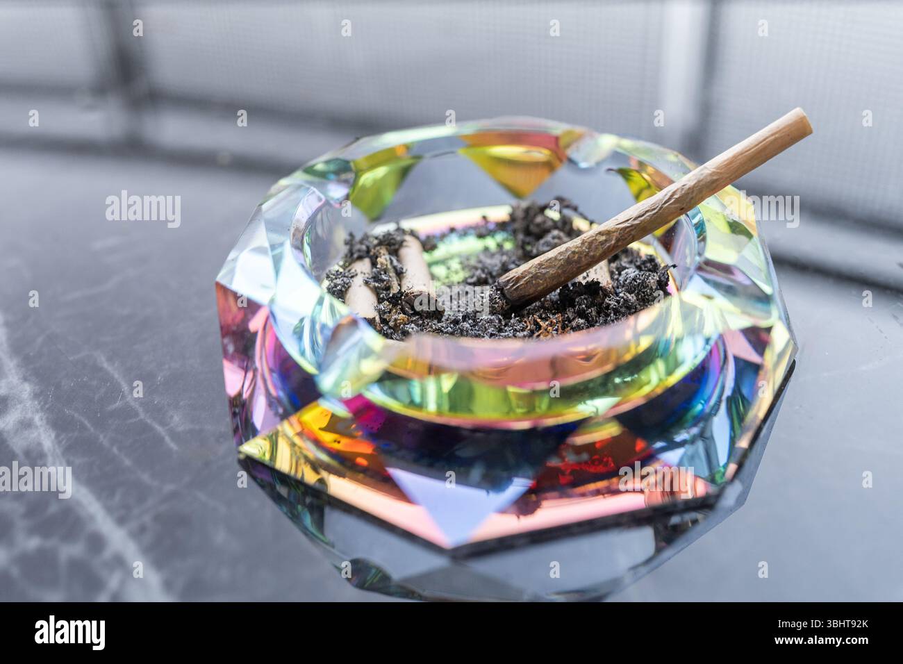 Posacenere luminoso con articolazioni di cannabis e cenere su un tavolo in marmo riflettente, catturato in un ambiente tranquillo per evocare relax, stile di vita e cultura contemporanea. Foto Stock