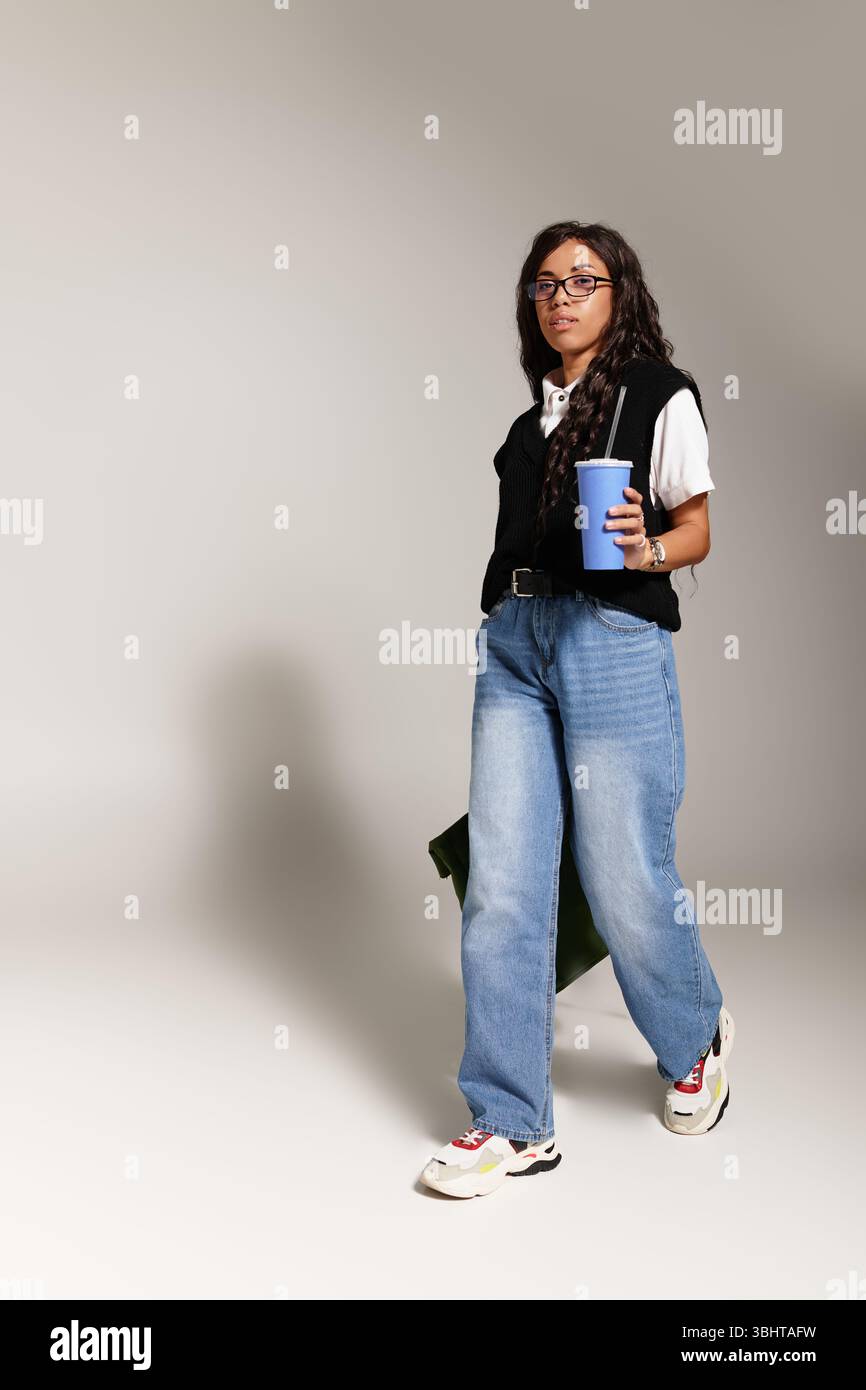 Una giovane donna con un abbigliamento casual si muove con sicurezza, gustando un vivace drink in mano. Foto Stock