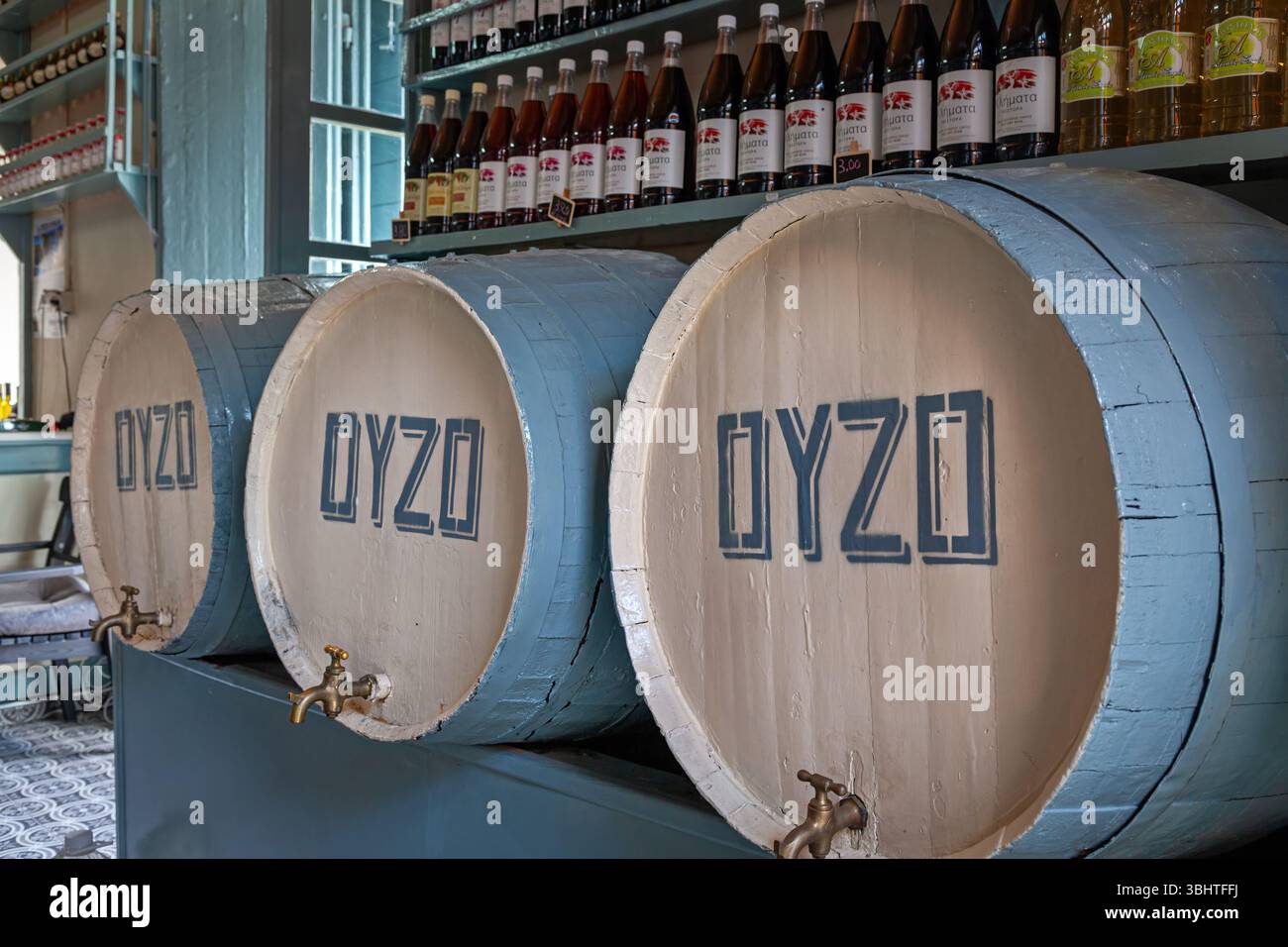Interno di una tradizionale distilleria greca con file di bottiglie di ouzo e botti di affinamento, che mettono in risalto l'artigianato locale e il patrimonio culturale. Foto Stock