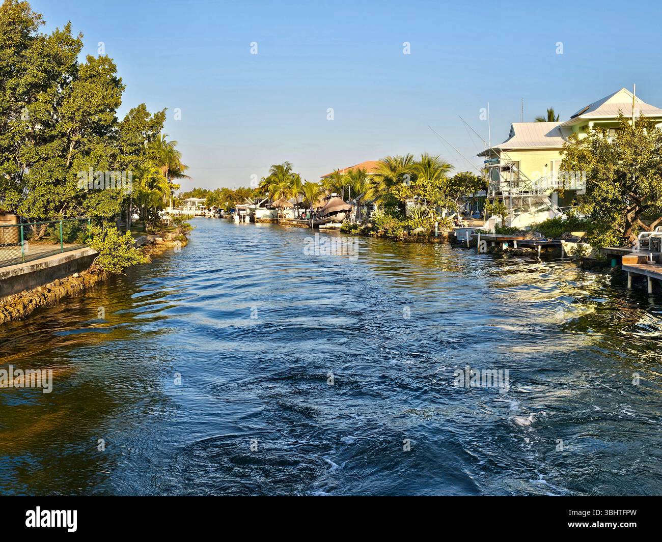 Stretto canale che conduce a un porticciolo, al porto di pescatori e al cantiere navale di Key largo, Florida. Il canale è fiancheggiato da case. Foto Stock