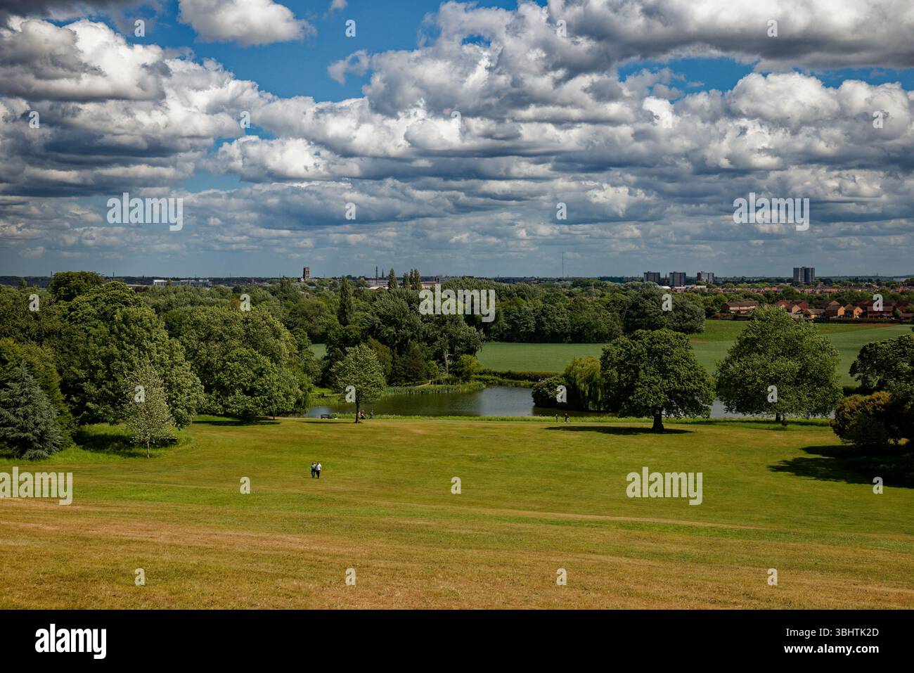 Una coppia inizia la passeggiata sulla collina a Cusworth Park con l'Upper Pond dietro di loro e lo skyline della città di Doncaster sullo sfondo. Foto Stock