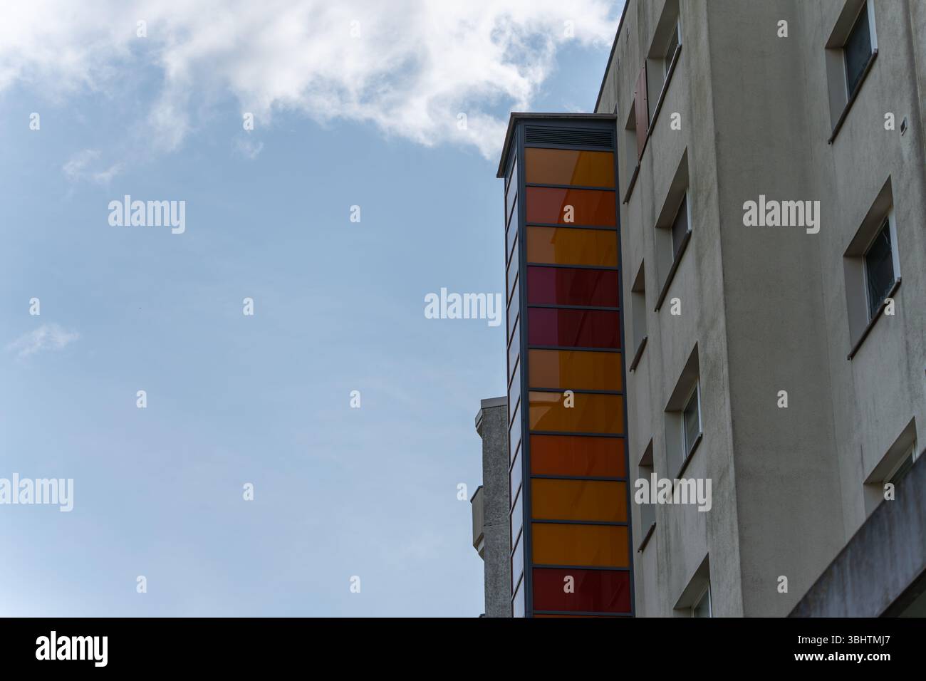 Un alto edificio con pannelli di vetro colorati sulla sua facciata. Il rivestimento in vetro si illumina in sfumature di rosso e arancione contro il cielo. Foto Stock