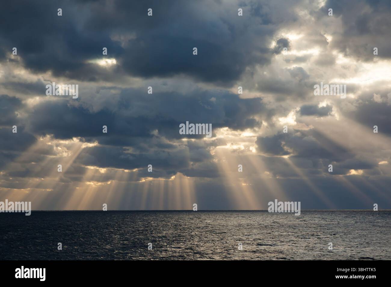I raggi del sole si fanno strada attraverso il cielo nuvoloso coperto dal mare aperto. Foto Stock