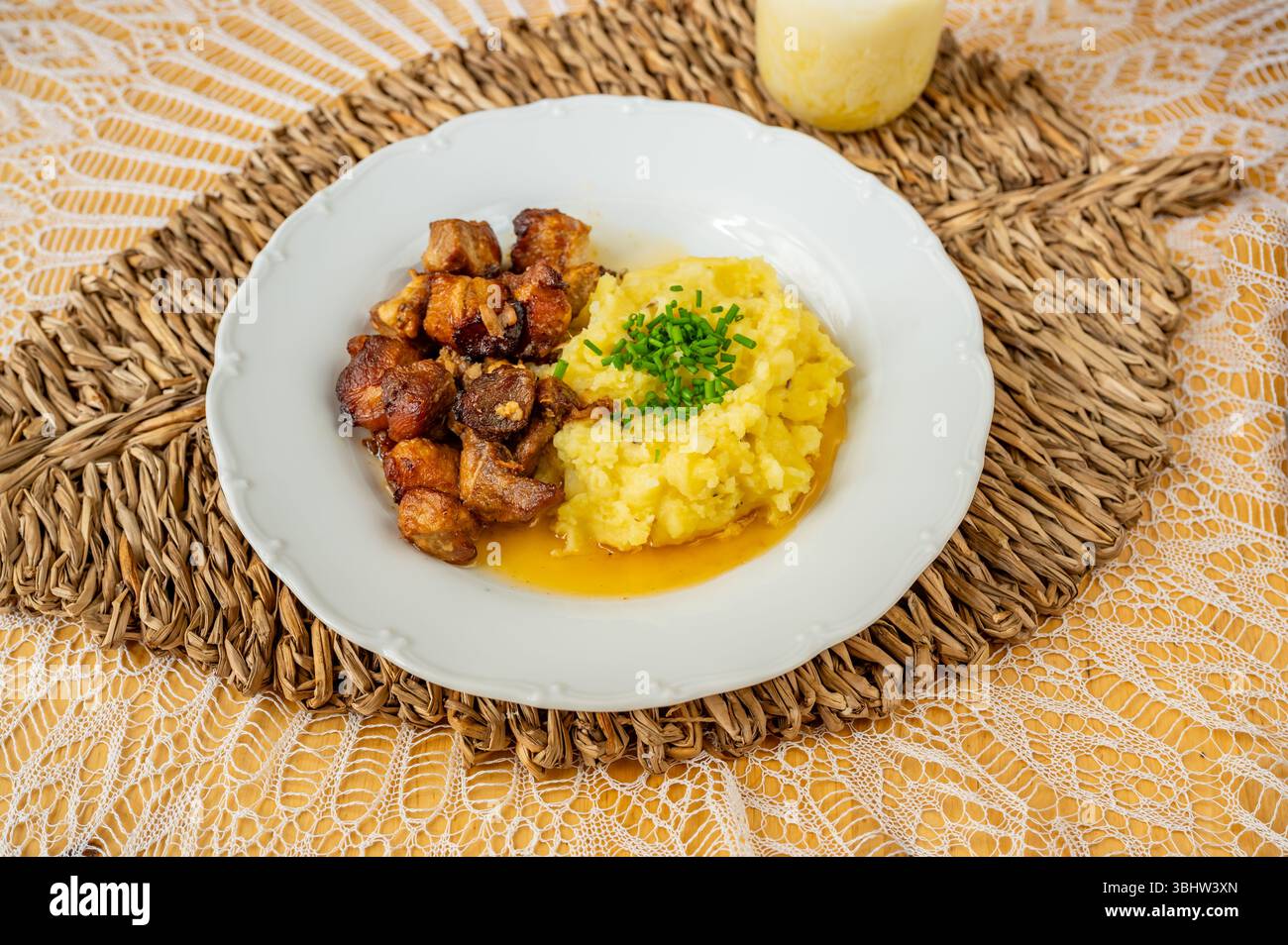 Pezzi di suino succoso cotti fino a quando non diventano dorati con purè di patate su un piatto bianco su un panno di bambù su una tovaglia di pizzo, frullato e primo piano. Foto Stock