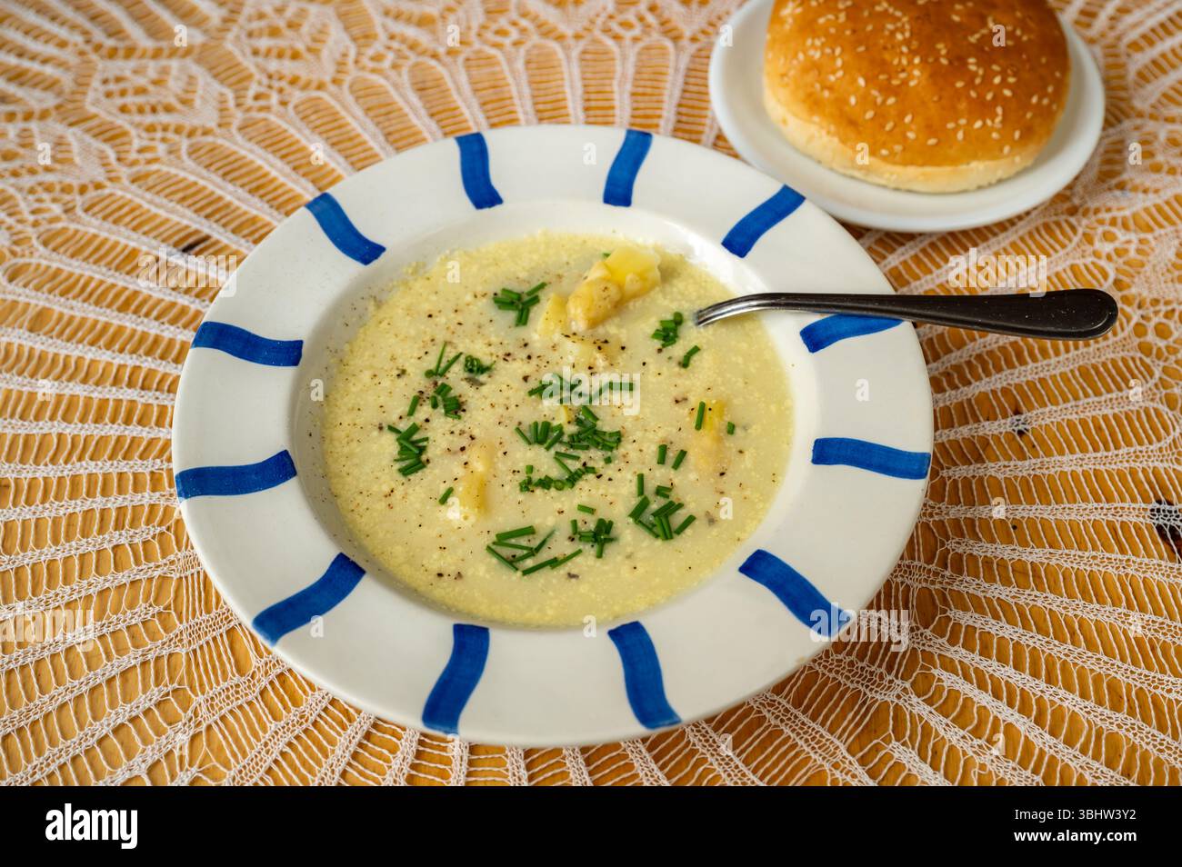 Zuppa densa di asparagi in piatto a strisce blu, cucchiaio e panino su tovaglia di lacy. Foto Stock