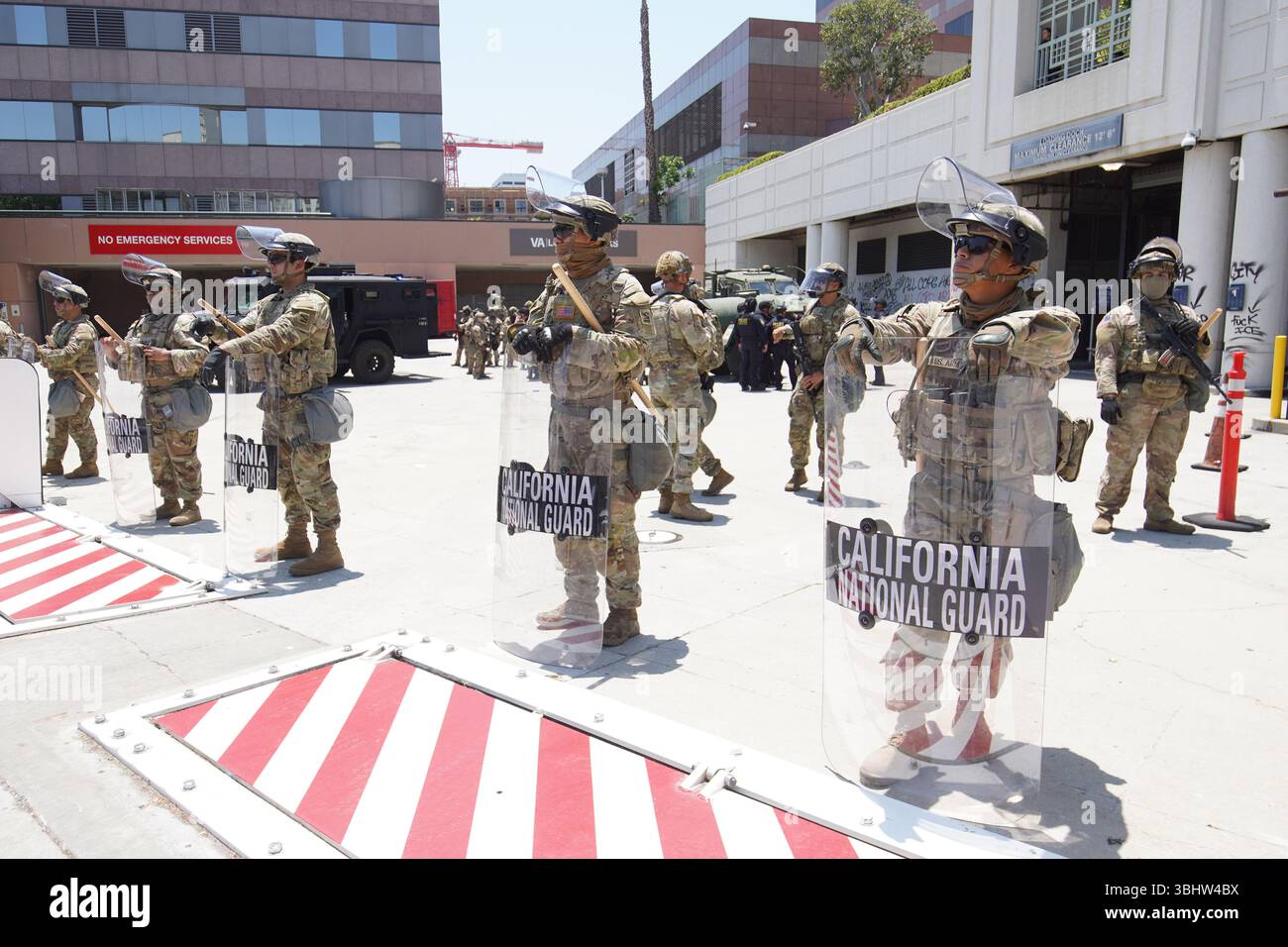 La polizia e la Guardia Nazionale della California stanno fuori dall'edificio federale con tutto il necessario. A Los Angeles, le proteste in corso contro le recenti incursioni DEL GHIACCIO si sono trasformate in intensi scontri tra i manifestanti e le forze dell'ordine. Le tensioni continuarono nella notte del 10 giugno, spingendo il sindaco Karen Bass a dichiarare lo stato di emergenza e imporre un coprifuoco in tutta la città, il primo dal 1992. I manifestanti si riunirono fuori dall'edificio federale del centro, dove gli ufficiali usavano granate stordenti e spray al pepe per disperdere la folla. Dozzine hanno bloccato la superstrada 101 prima di essere sgombrato dalla pattuglia autostradale. Come saccheggio e p Foto Stock