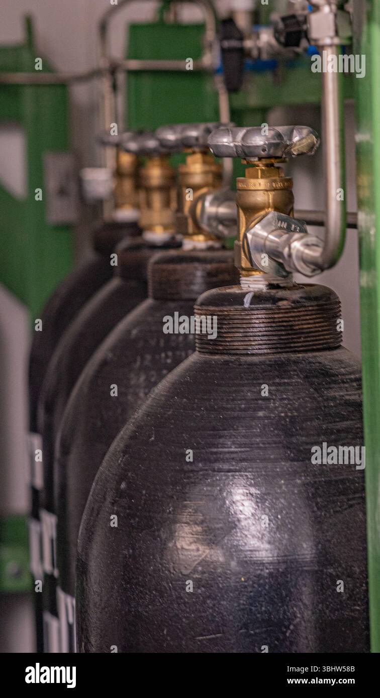 La foto mostra una fila di cilindri di aria compressa in metallo nero collegati a un sistema di tubi e valvole. I cilindri sono etichettati con "ARIA COMPRESSA" e con Foto Stock