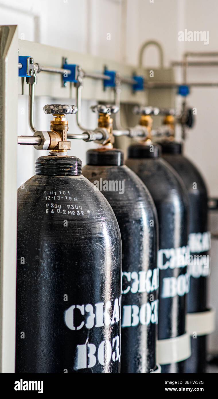 La foto mostra una fila di cilindri di aria compressa in metallo nero collegati a un sistema di tubi e valvole. I cilindri sono etichettati con "ARIA COMPRESSA" e con Foto Stock