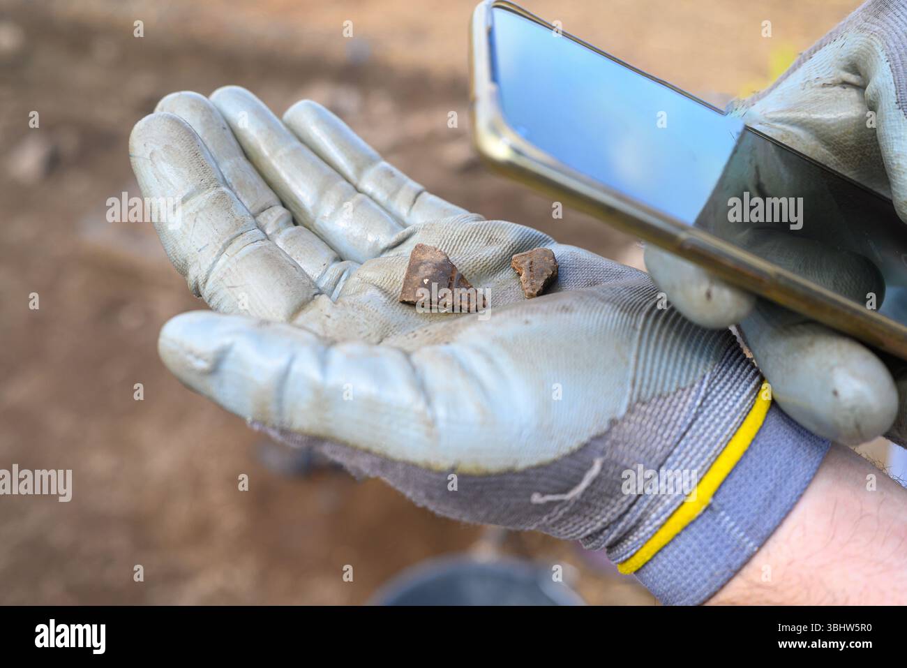 Archeologo che documenta gli artefatti con uno smartphone presso il sito di scavo. Foto Stock