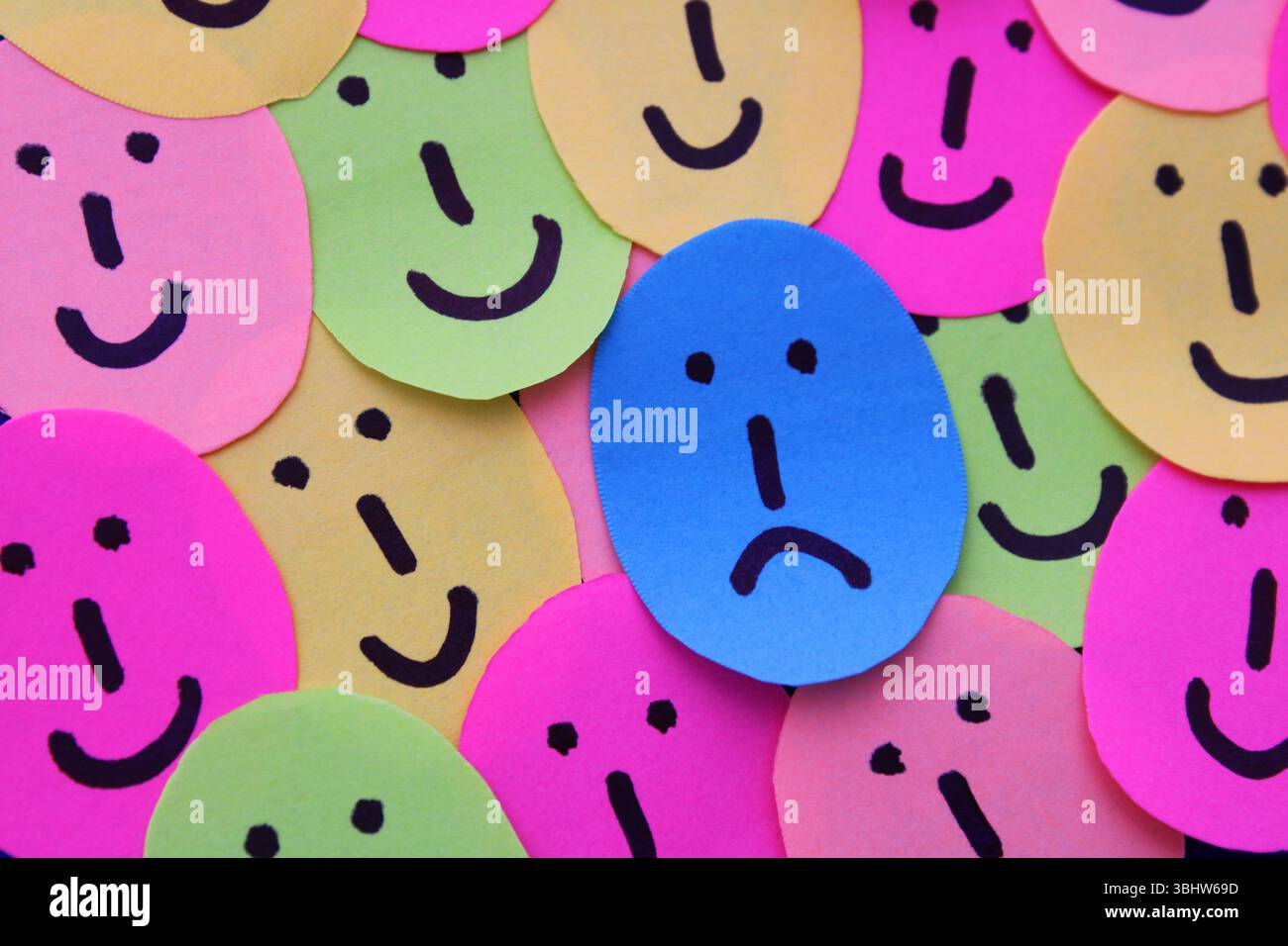 Una triste faccia blu tra molte facce felici Foto Stock