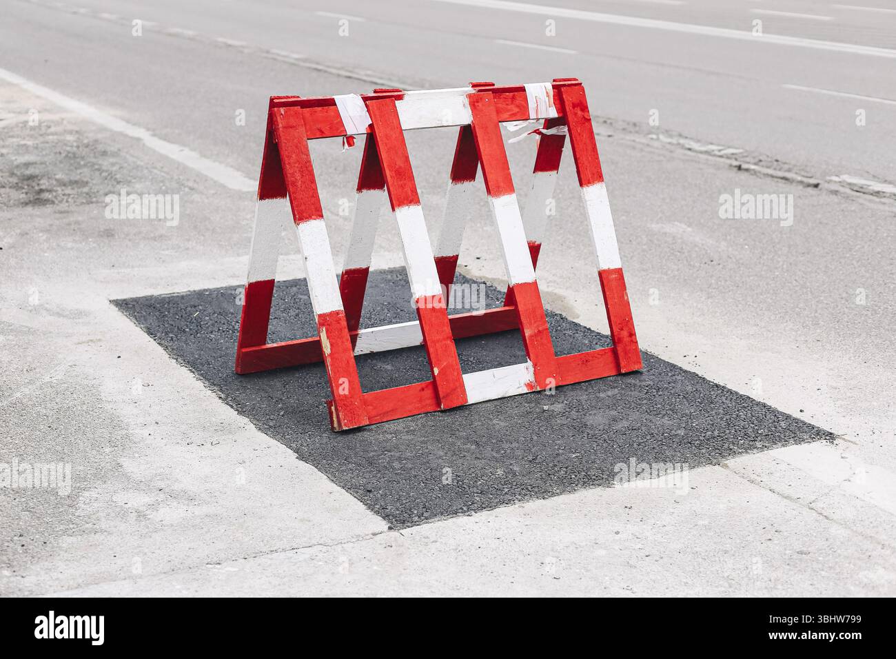 Barriera stradale rossa bianca. Recinzione di avvertenza su asfalto. Protezione della zona di costruzione. Concetto di sicurezza per il controllo del traffico. Elemento del cantiere urbano. Foto Stock