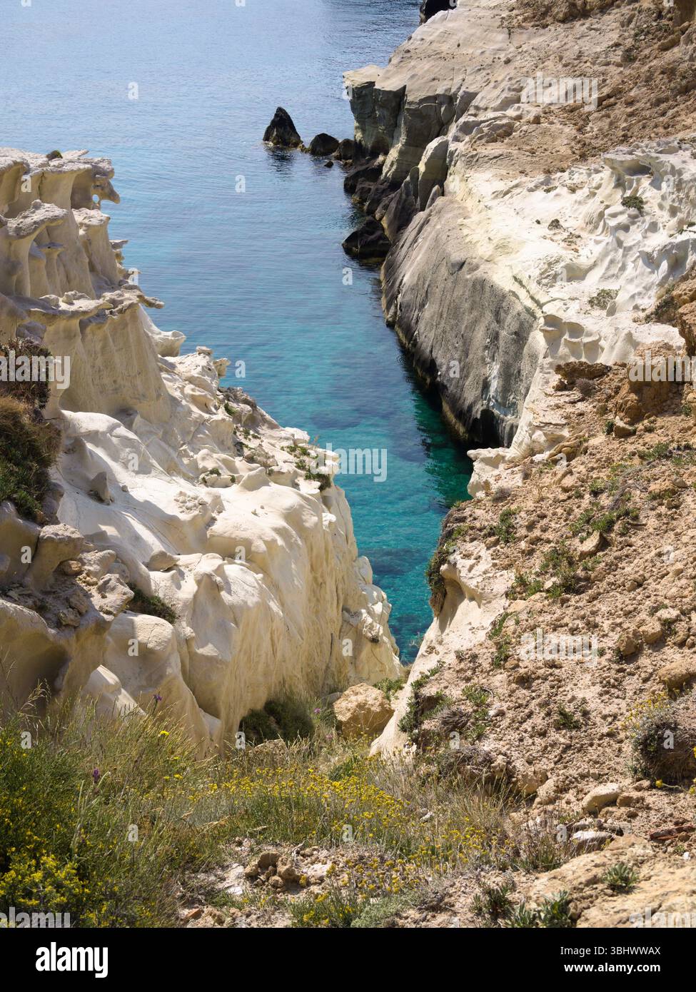 Scogliere luminose e acque turchesi lungo la costa vicino alla spiaggia di Sarakiniko sull'isola di Milos, in Grecia. Foto Stock