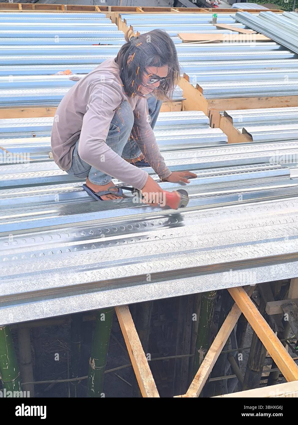 Un operaio edile sta tagliando lastre di zinco per la base in calcestruzzo del secondo piano di un edificio Foto Stock