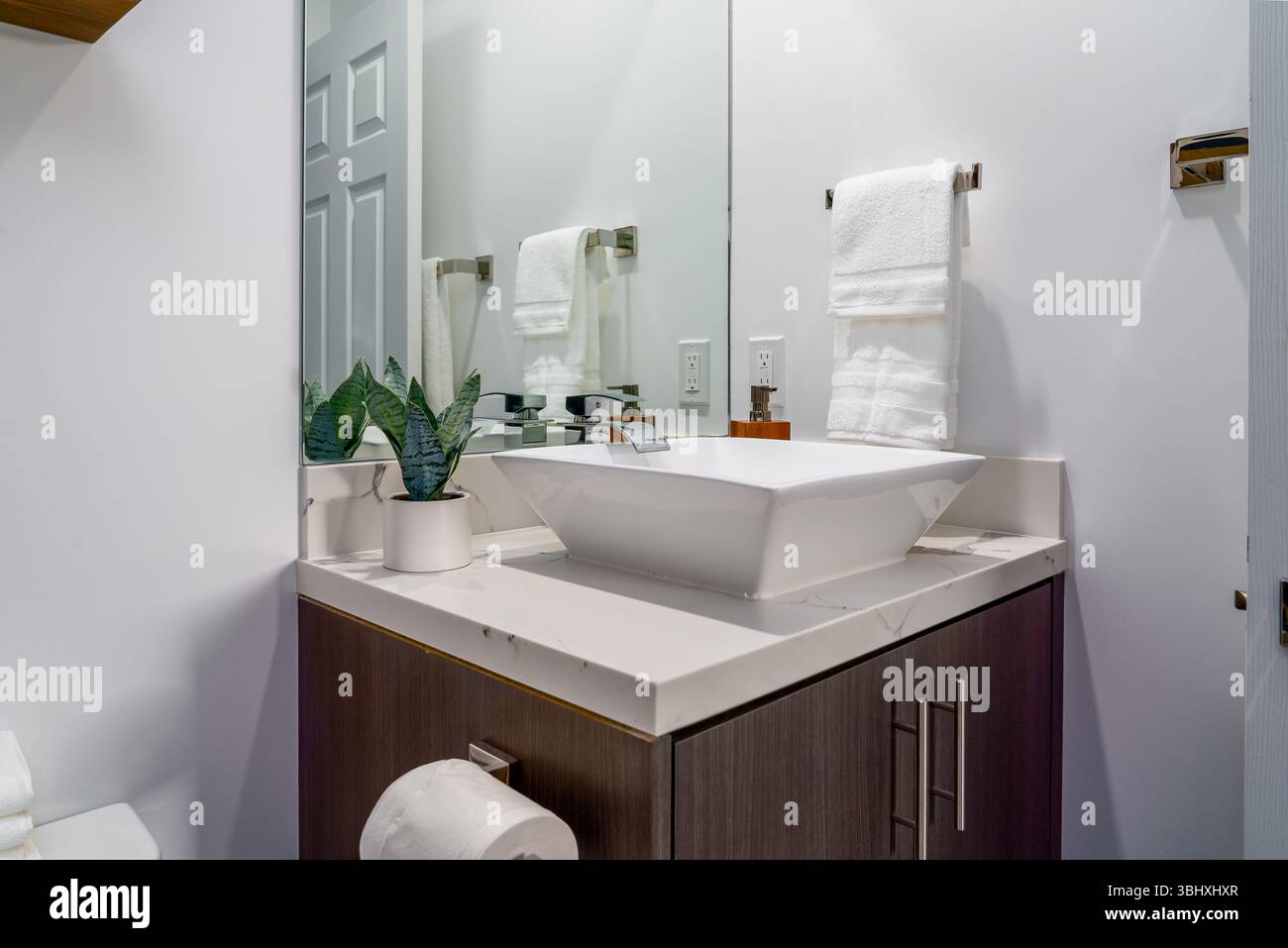 Bagno moderno con lavabo bianco e rubinetto con armadietto in legno e specchio Foto Stock